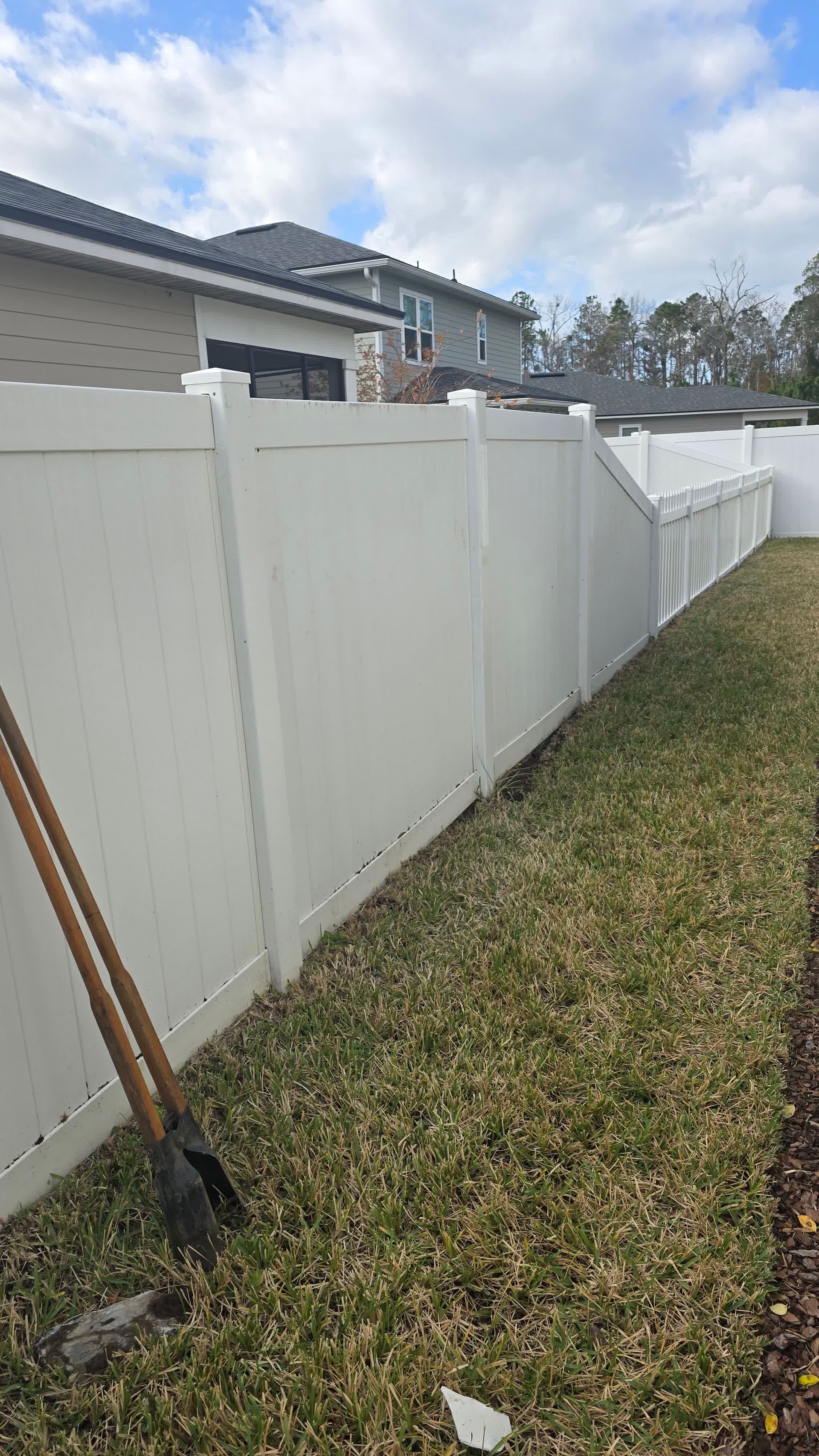 Stack of vertical slat replacement fence panels in a residential backyard, prepared for installation.