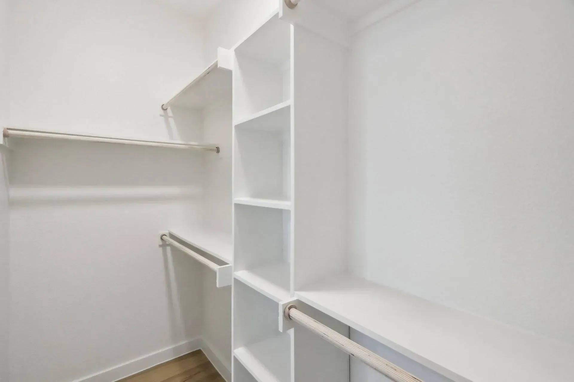Empty, white closet with built-in shelves and rods.