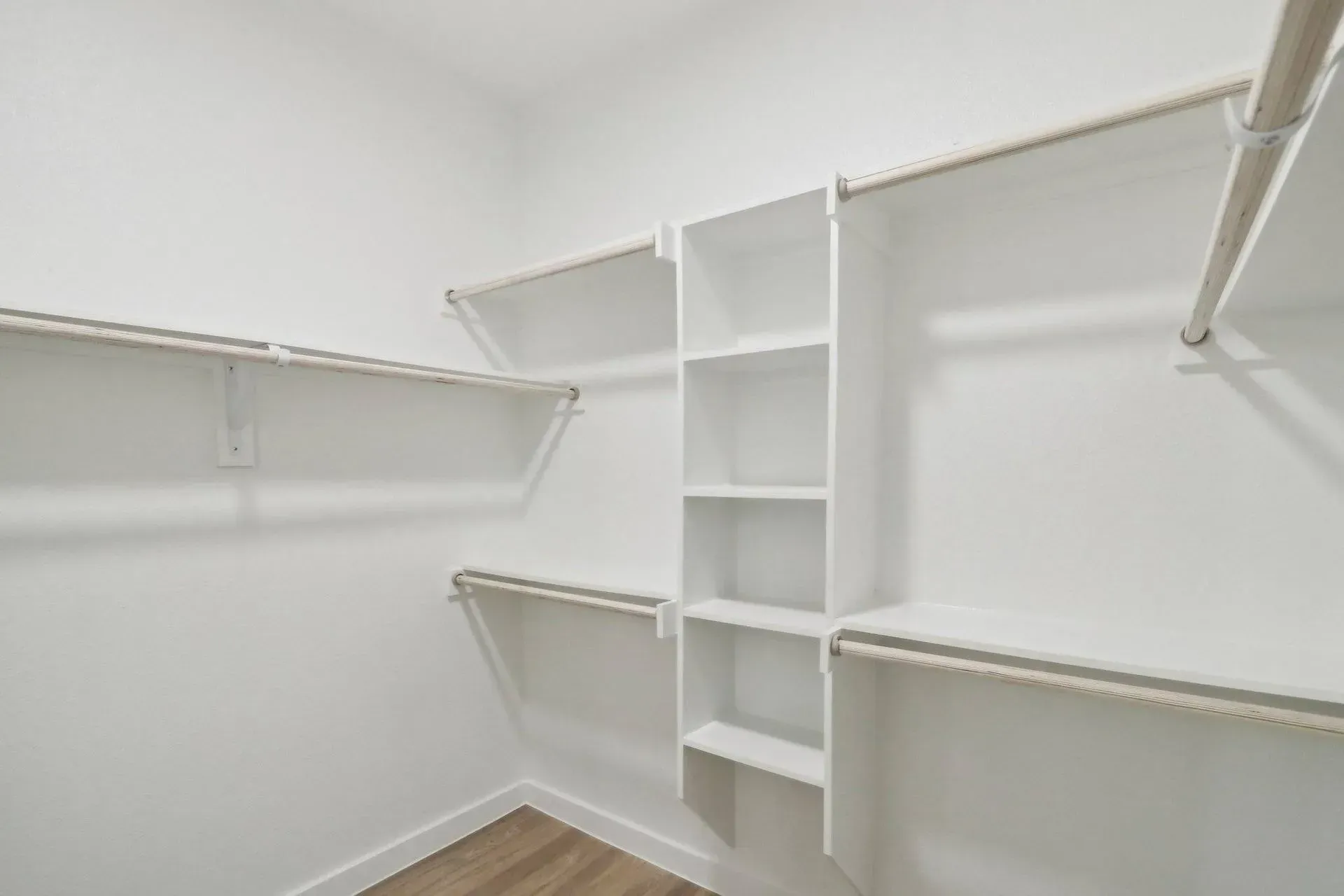 White walk-in closet with shelves and rods, built-in shelving unit, neutral colors.