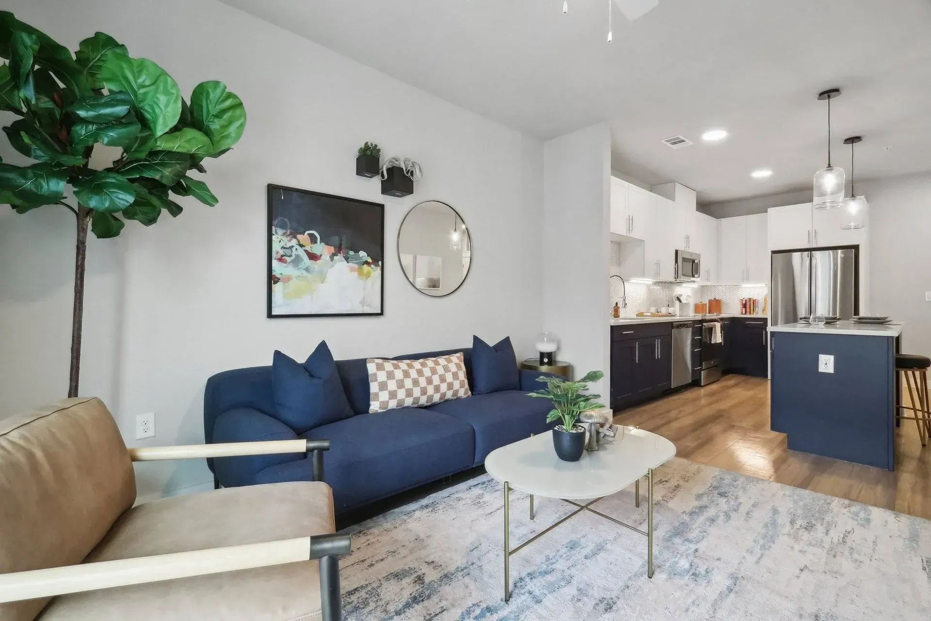 Living room with navy blue sofa, light wood chair, and open kitchen with island.
