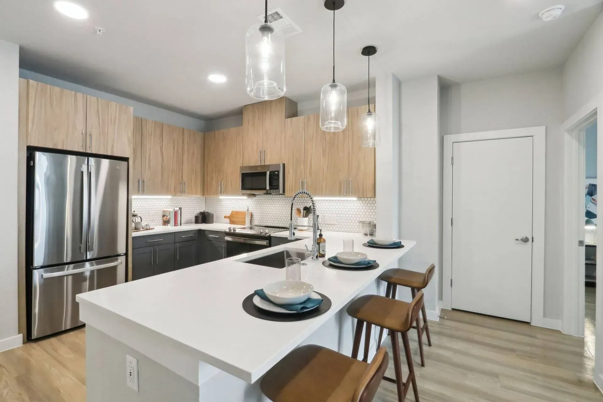 Modern kitchen with light wood cabinets, stainless steel appliances, and a white countertop island with bar stools.