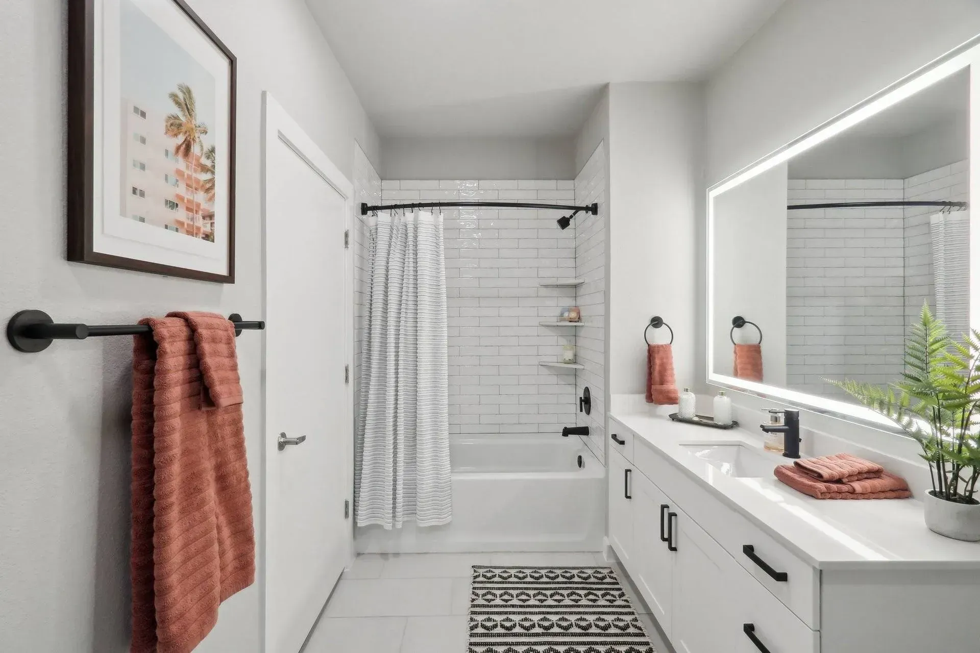 Modern white bathroom with black accents: vanity, towel rack, shower rod, and door hardware.