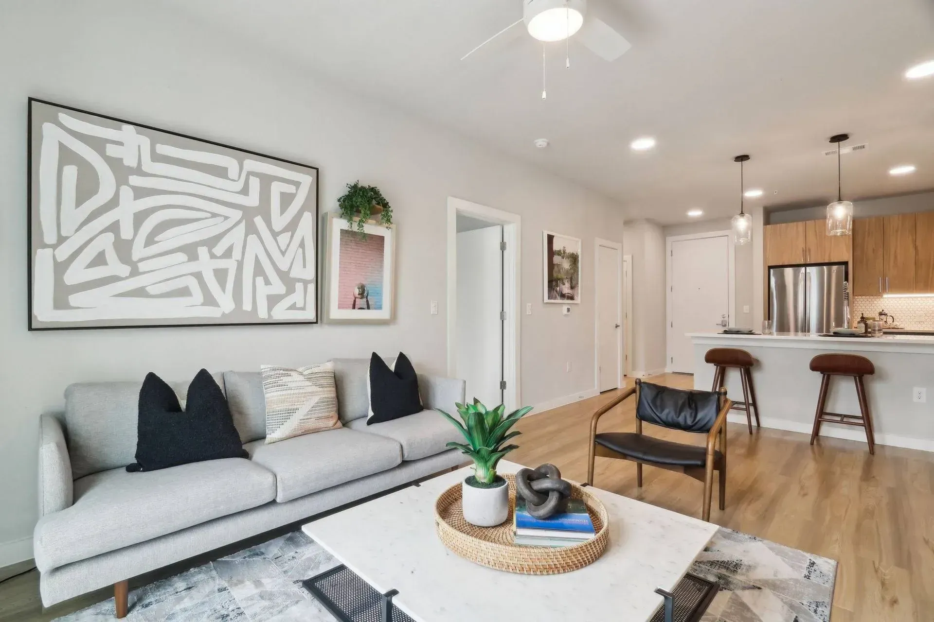 Modern living room with light gray sofa, abstract art, and kitchen in background.