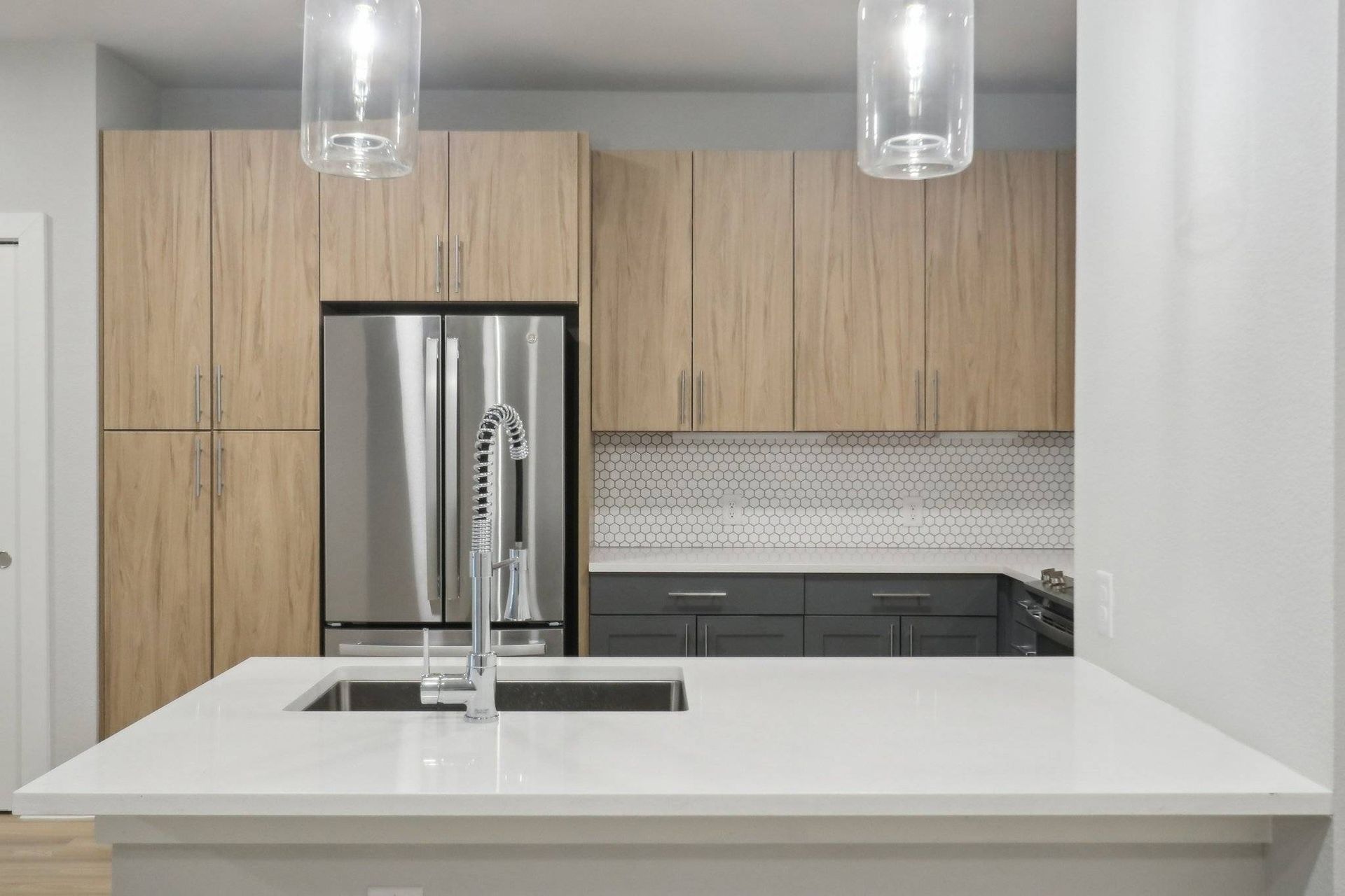 Modern kitchen with island, wood upper cabinets, stainless steel fridge, and white countertops.