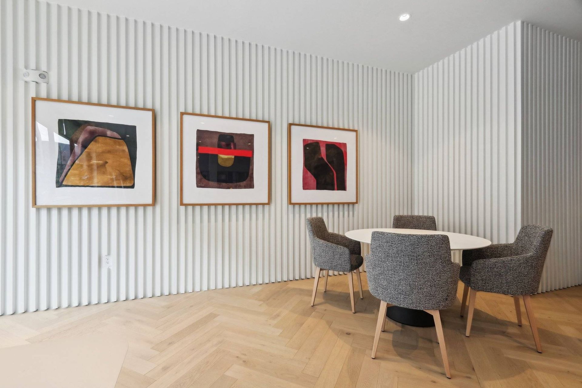 Modern resident lounge with a round table, four gray chairs, and abstract framed art.
