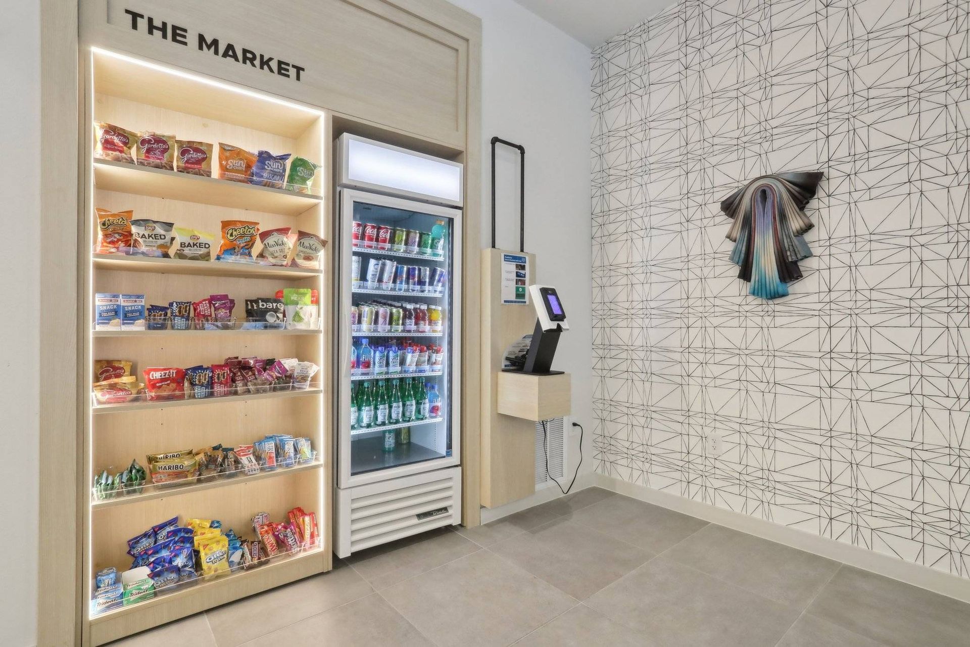 Communal market area with snack shelves, a vending machine, and a touch-screen kiosk.