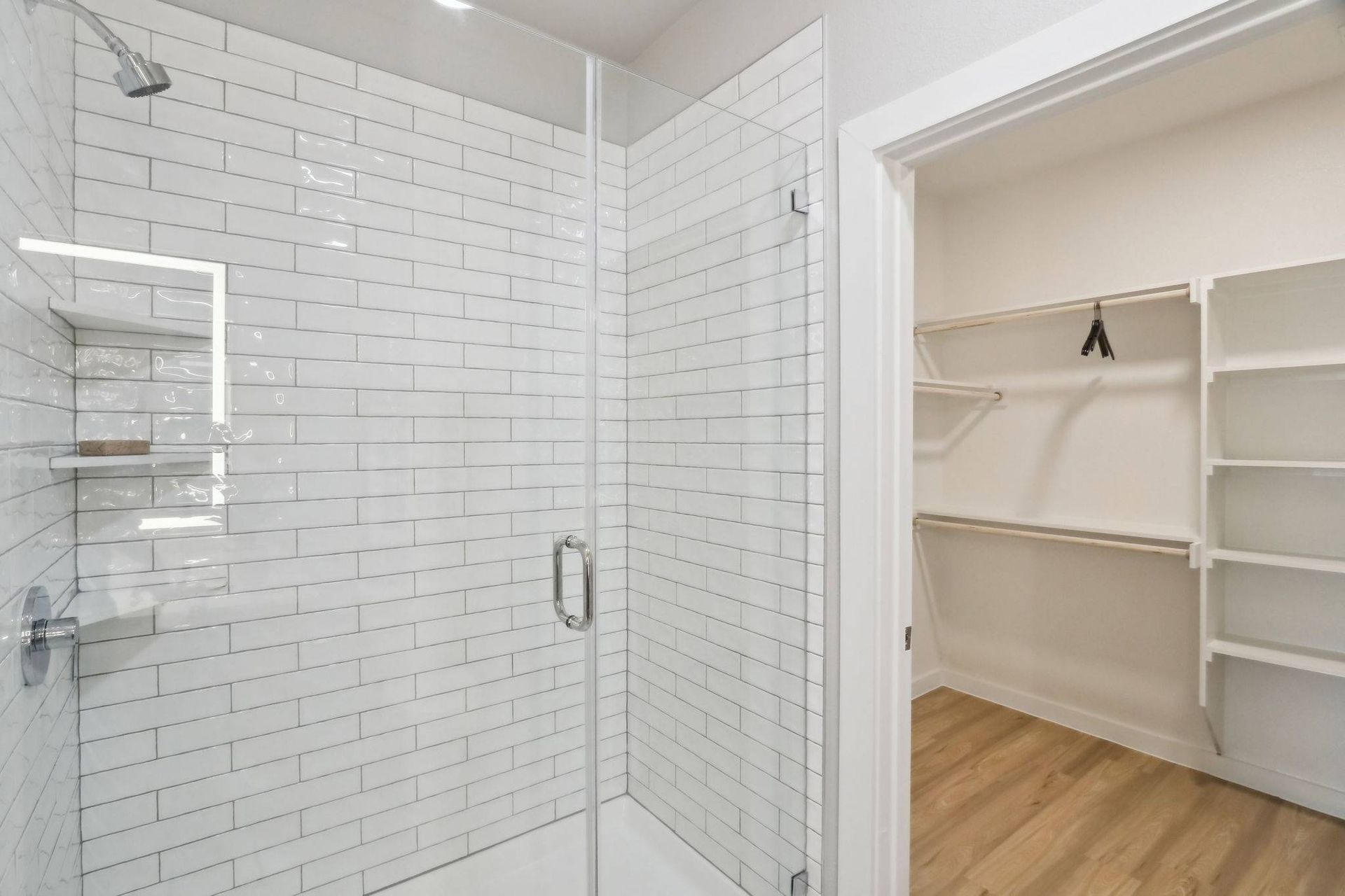 Bathroom shower with glass door and white subway tiles; adjacent walk-in closet with shelving.
