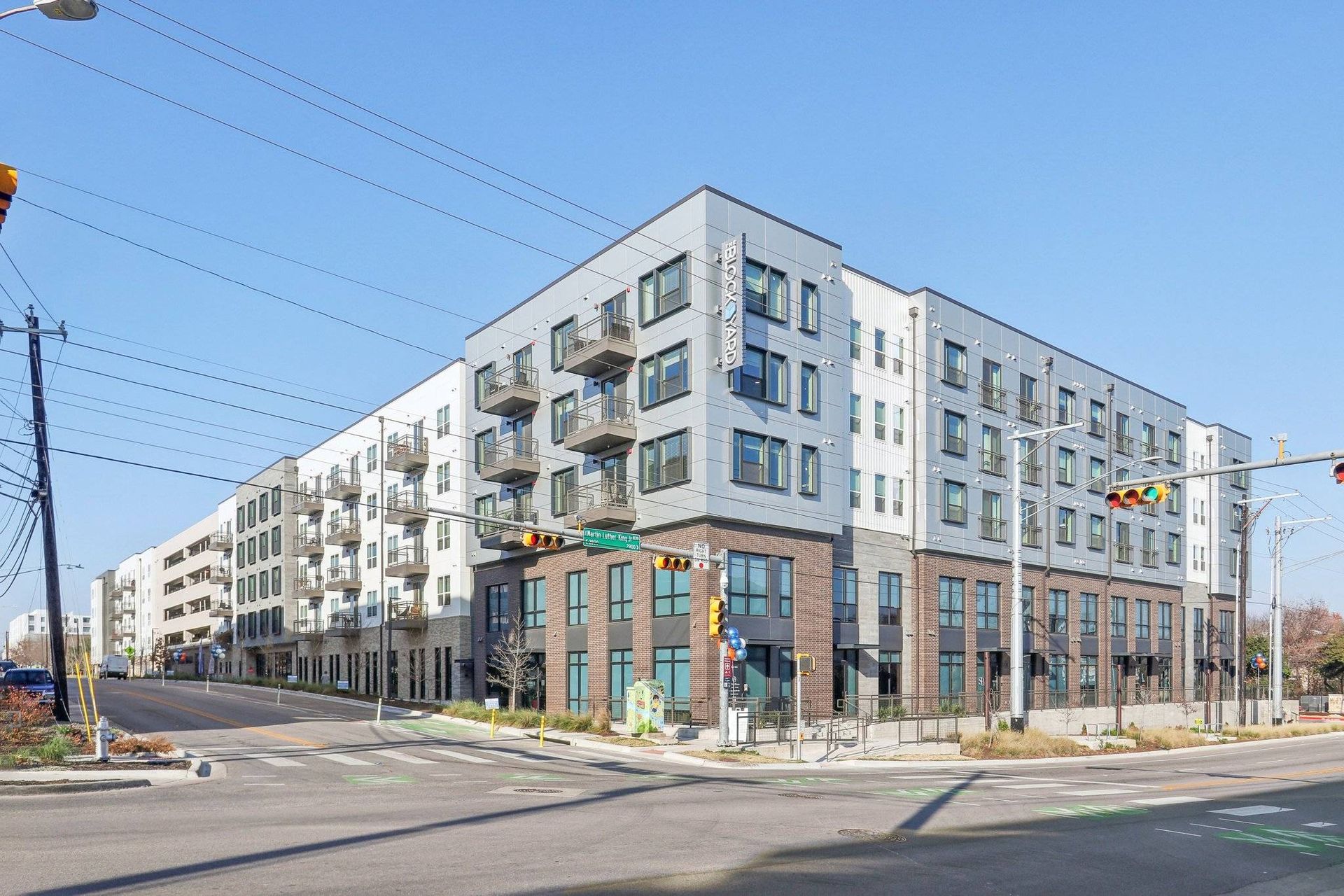 Exterior view of a modern multi-story apartment building at a street corner with balconies.