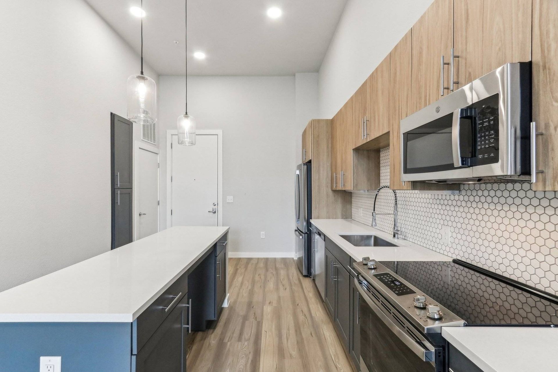 Modern apartment kitchen with island, stainless steel appliances, and wood-tone cabinets.