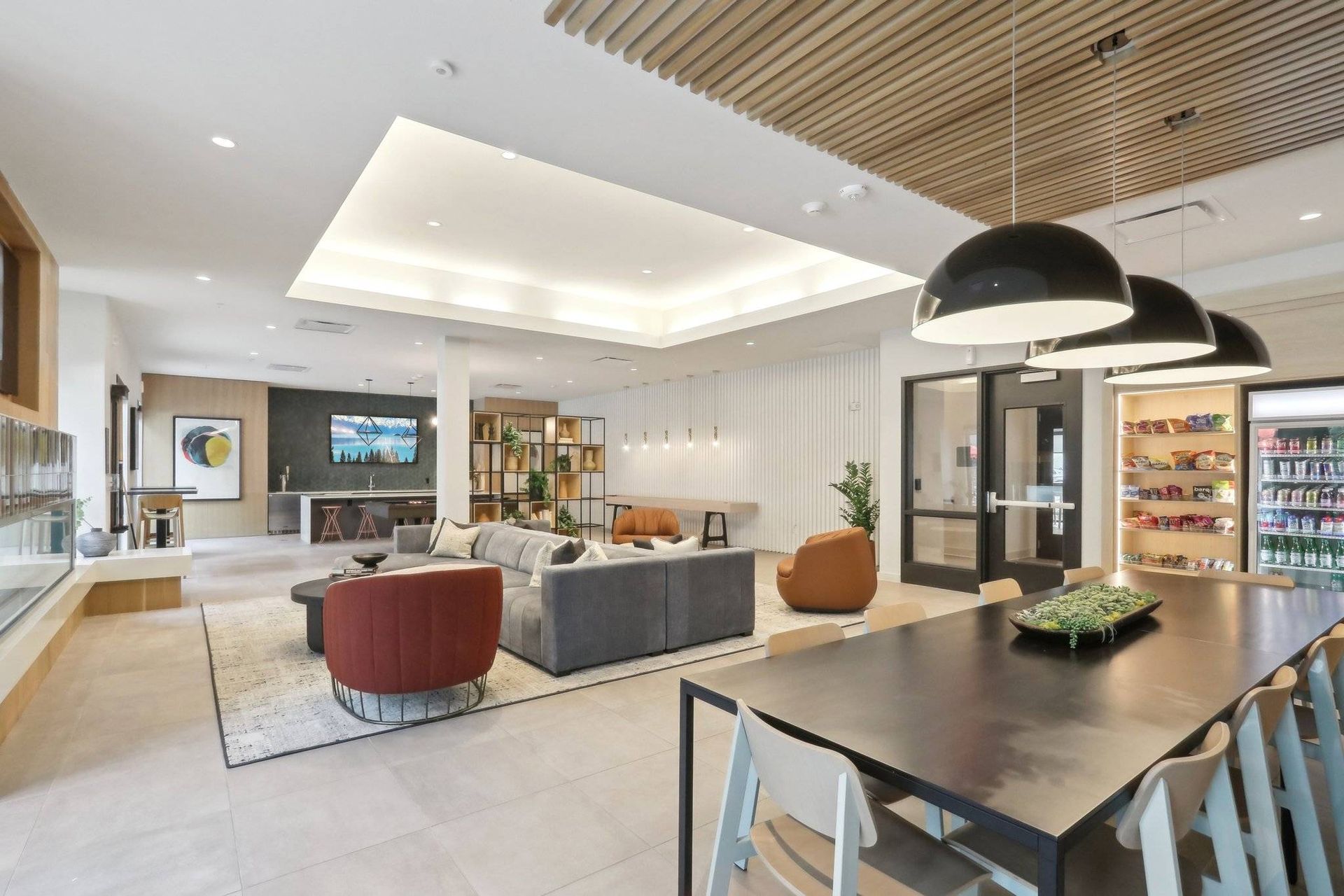 Spacious resident lounge with gray sectional sofa, lounge chairs, and a long dining table.