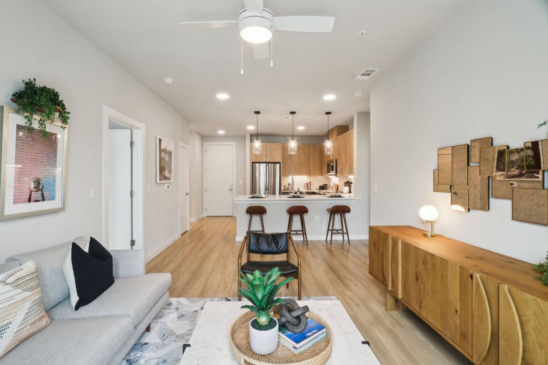 Open-concept living area with gray sofa, marble coffee table, and a kitchen island with three brown stools.