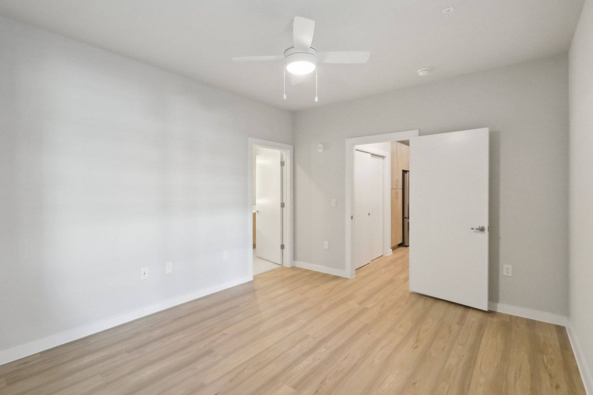 Empty bedroom with light wood floors, white walls, a ceiling fan, and open doors.