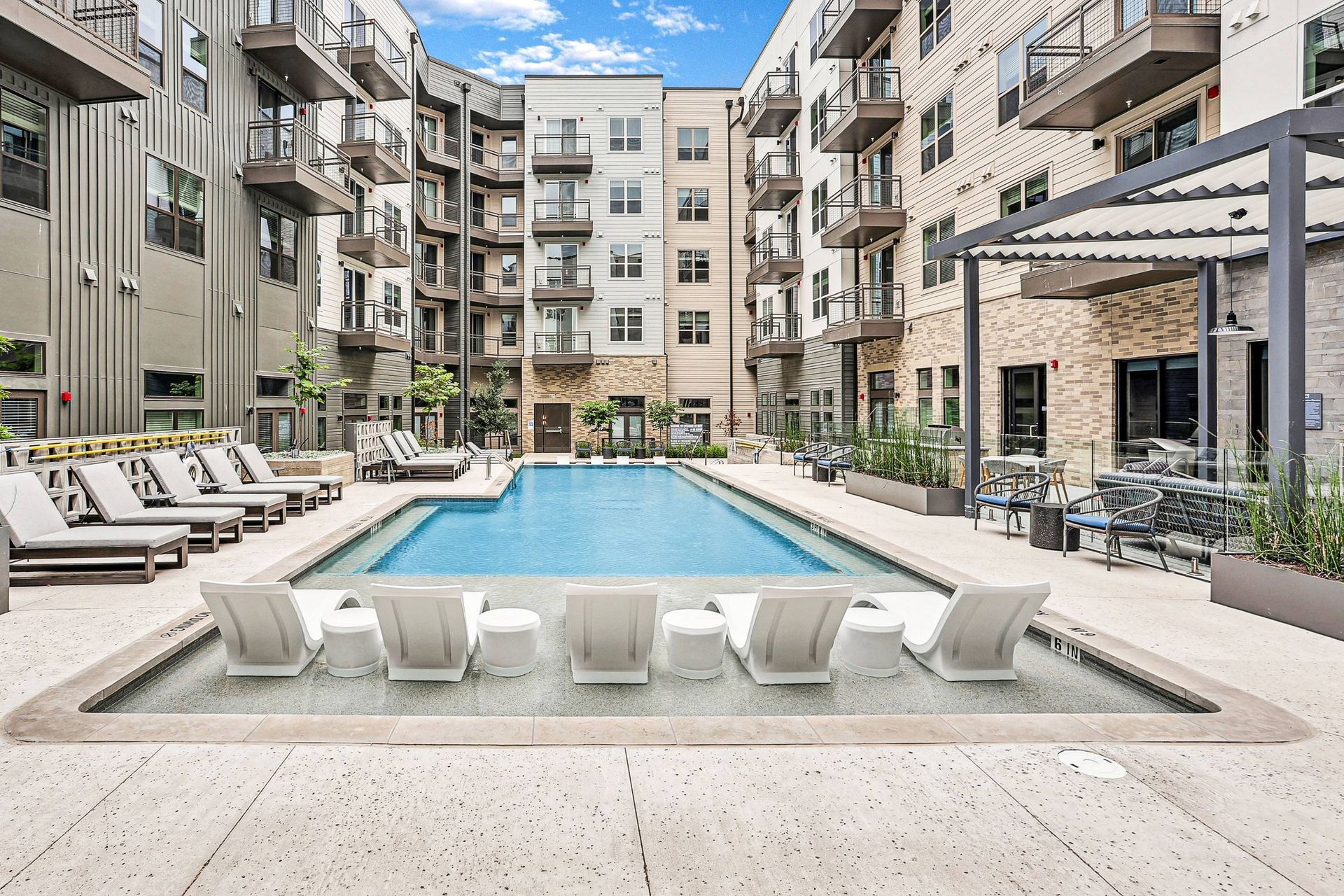 Outdoor communal pool area surrounded by apartment buildings with white lounge chairs.
