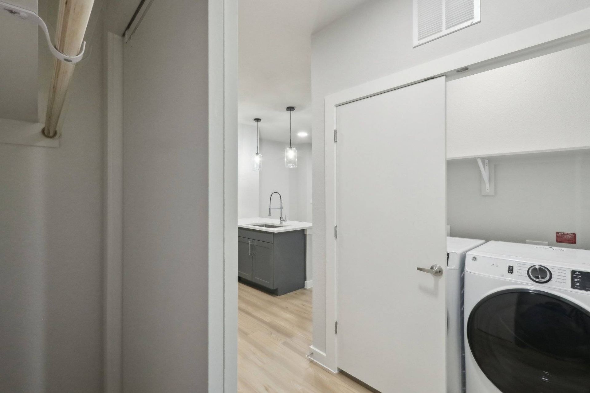 Laundry closet with a front-loading washer and dryer; view into a modern kitchen island.