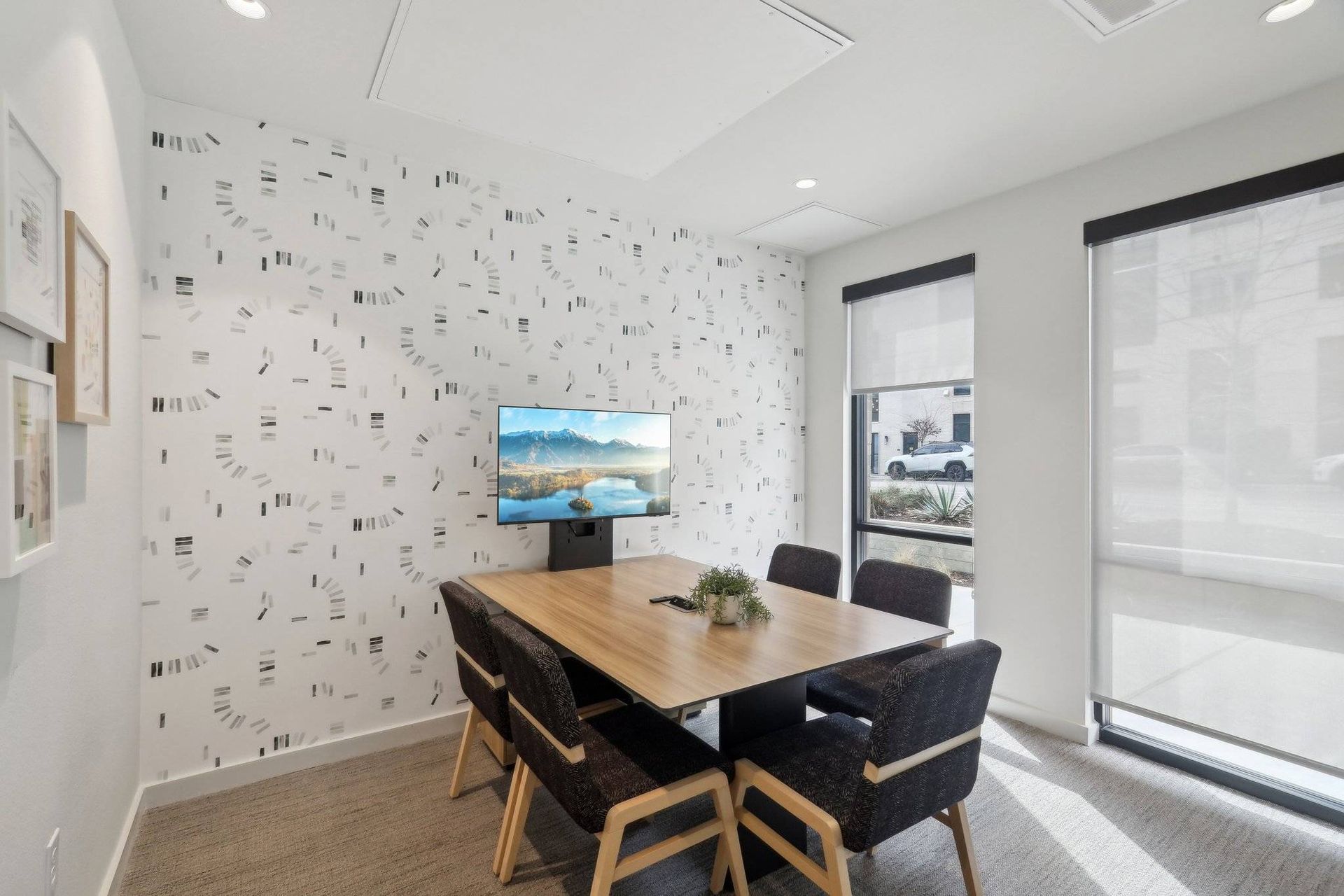 Conference room with wooden table, six chairs, monitor, and patterned wallpaper.
