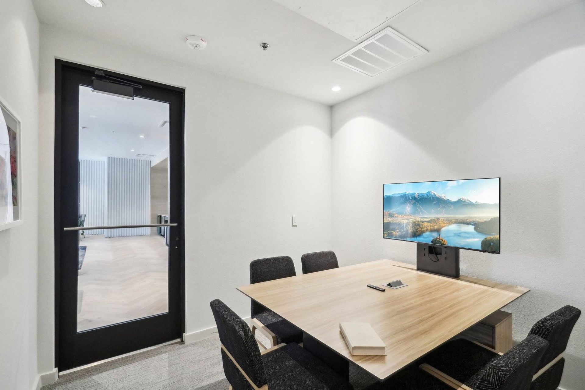 Small conference room with a wooden table, several chairs, and a wall-mounted monitor.