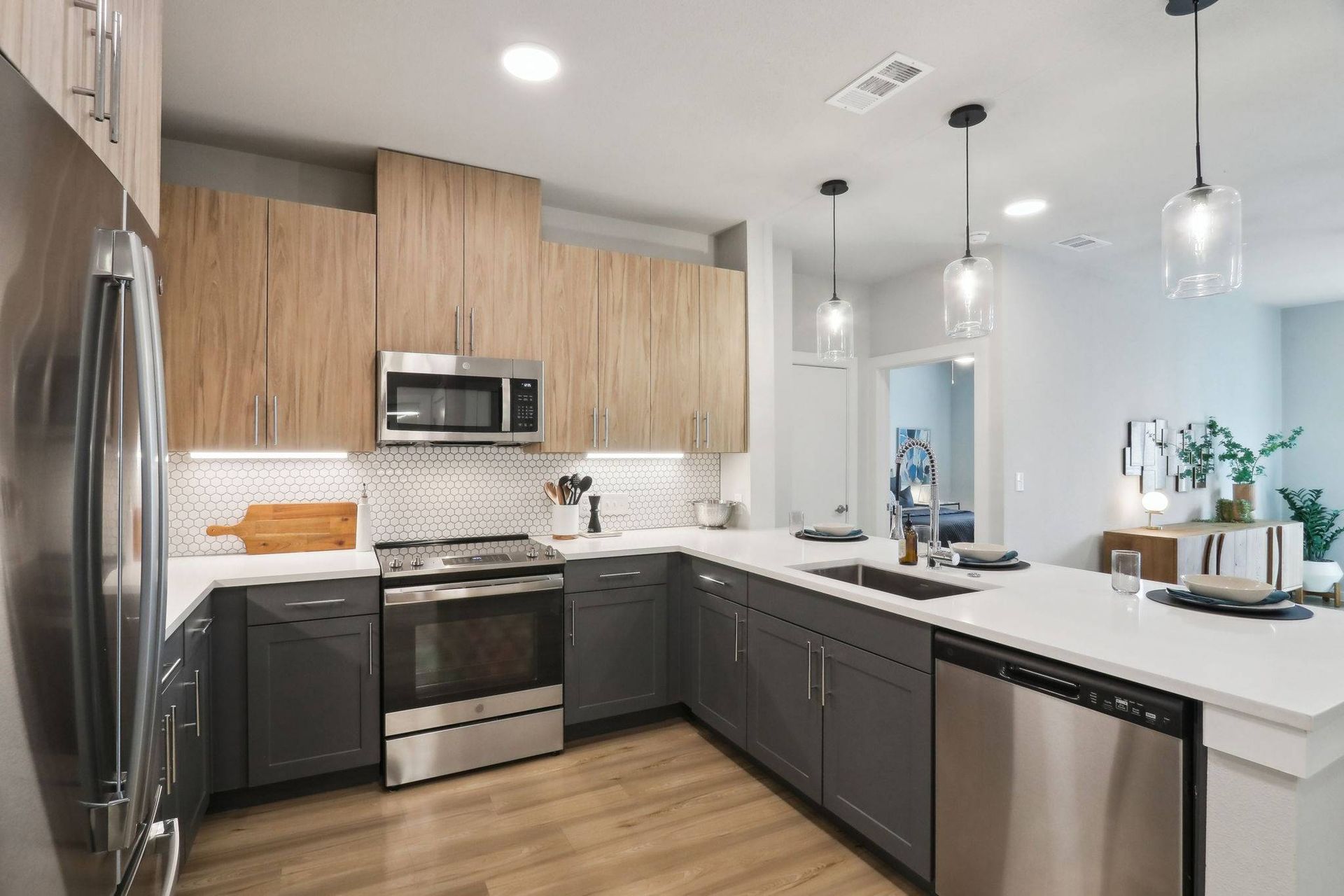 Modern kitchen with gray lower cabinets, light wood upper cabinets, white countertops, and stainless steel appliances.