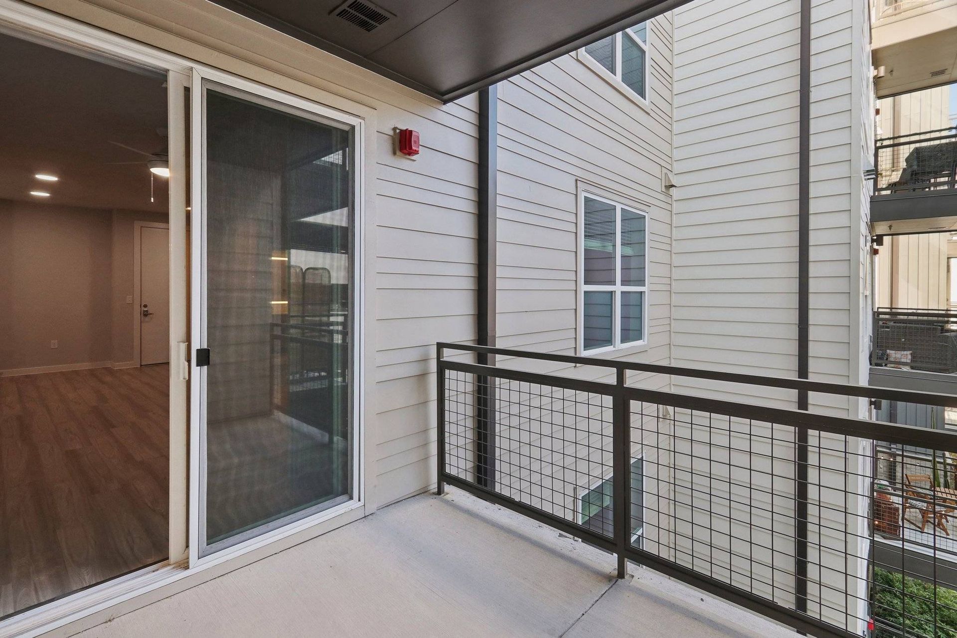 Balcony with sliding glass door, metal railing, and beige exterior siding.