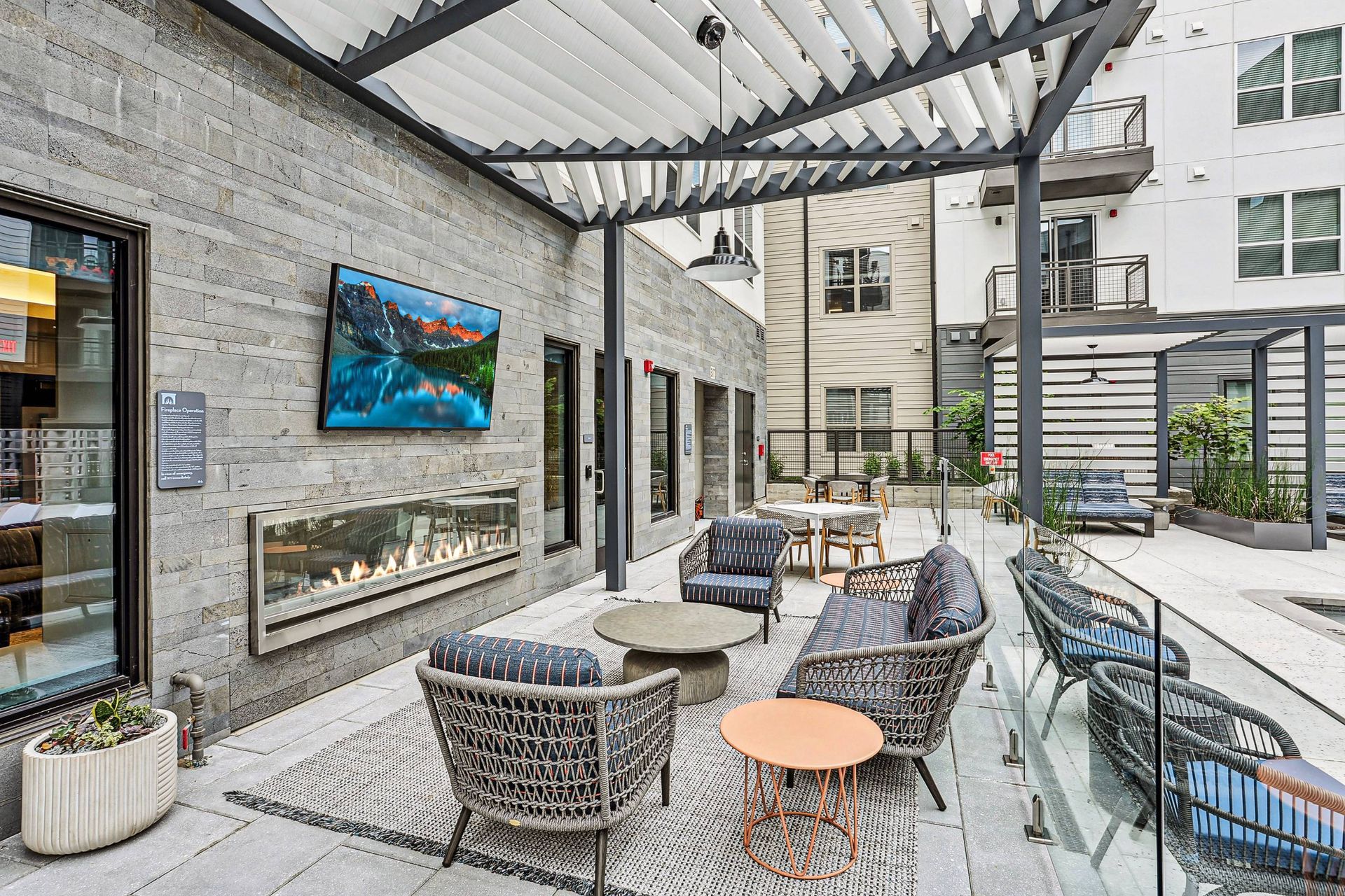 Outdoor community lounge with a fireplace, TV, and seating under a pergola.