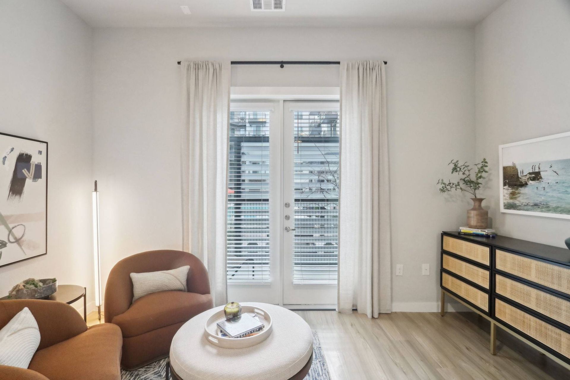 Living room with brown curved sofa, round coffee table, and French doors to balcony.