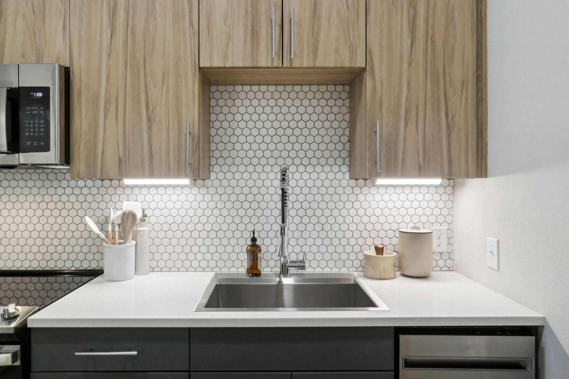 Modern kitchen with a stainless steel sink, hexagonal tile backsplash, and wooden cabinets.