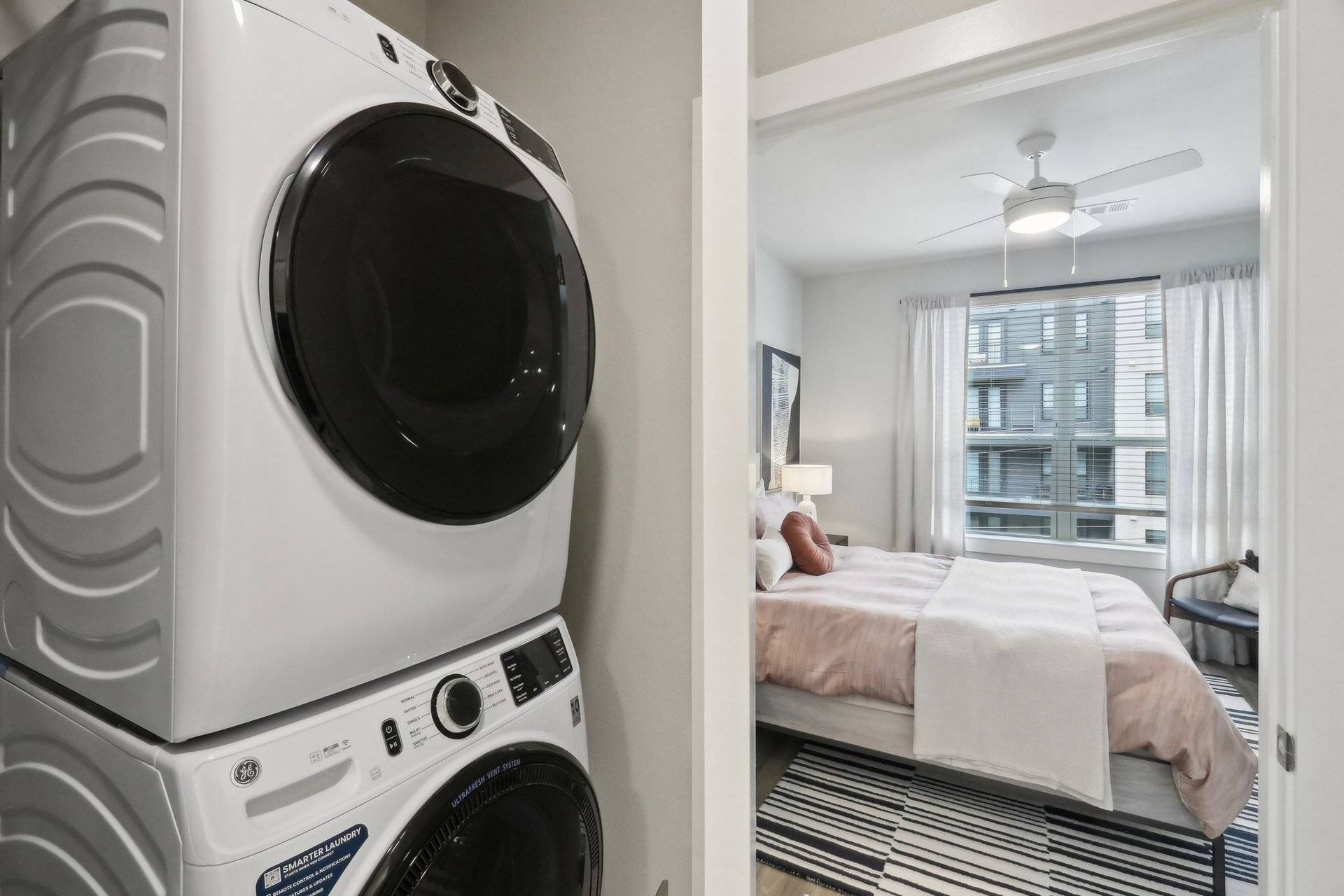 In-unit laundry closet with stacked washer and dryer beside a bedroom.