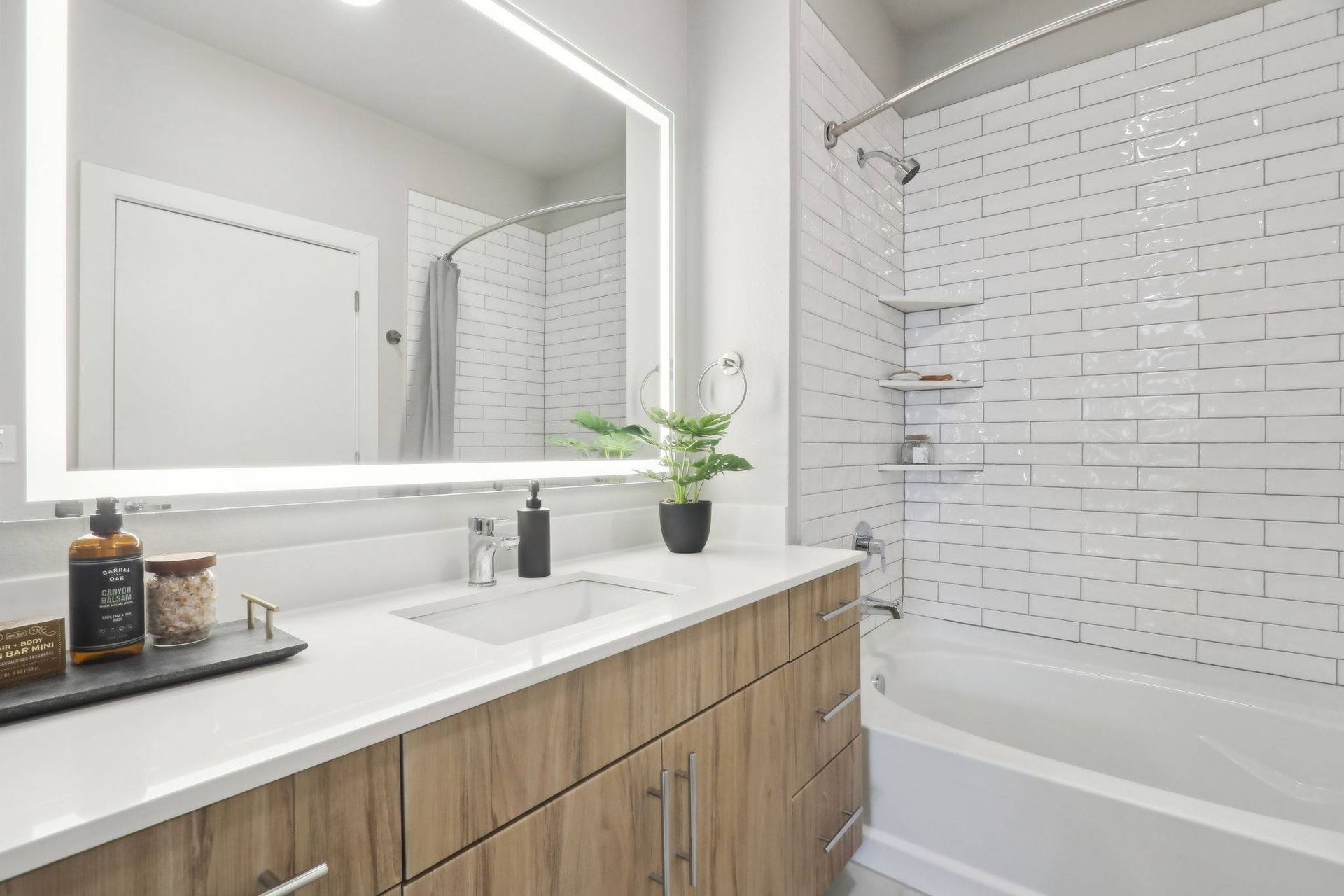 Modern bathroom with white subway tile, wooden vanity, and backlit mirror.