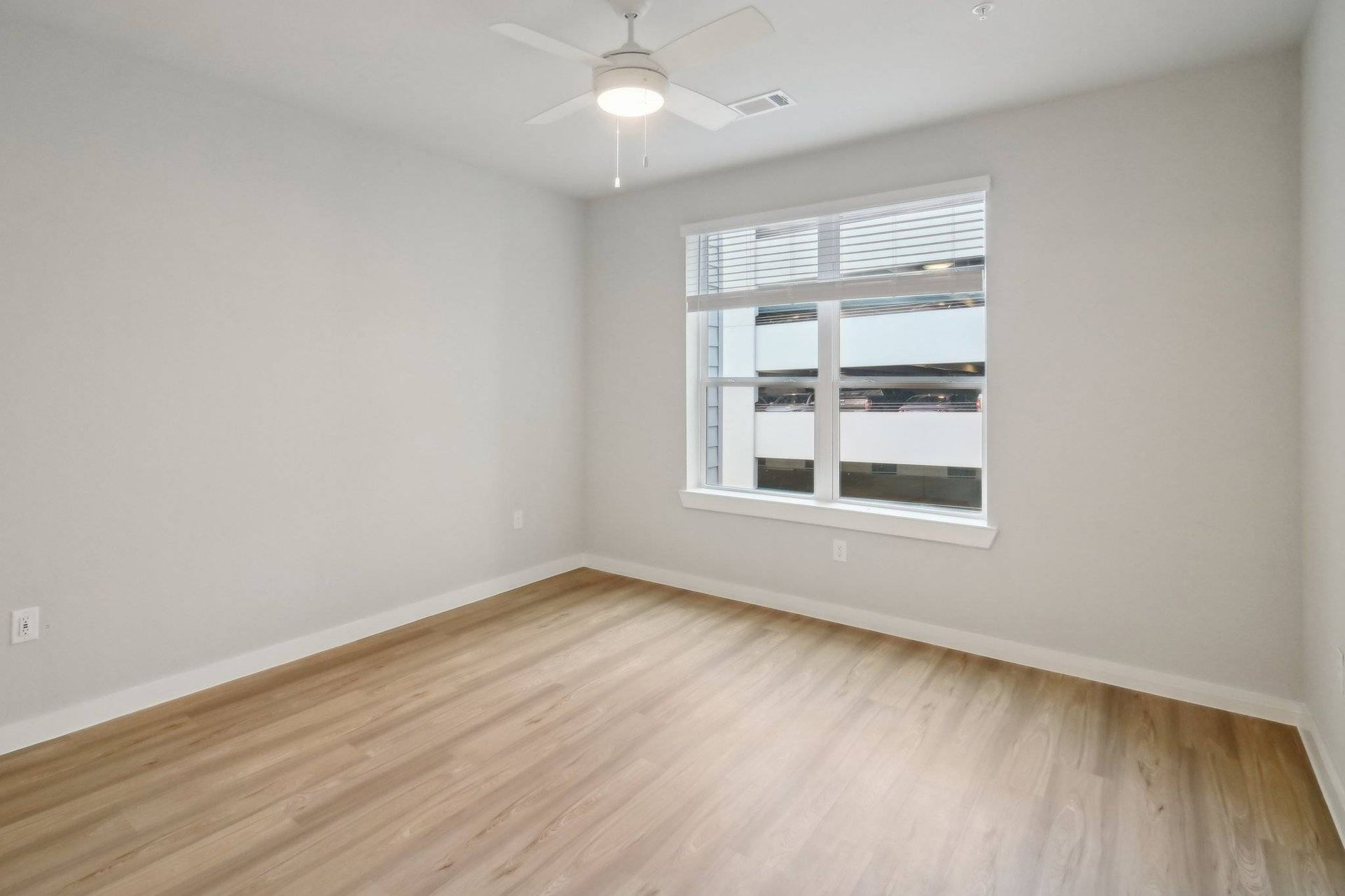 Empty room with light wood flooring, neutral walls, a window, and a ceiling fan.