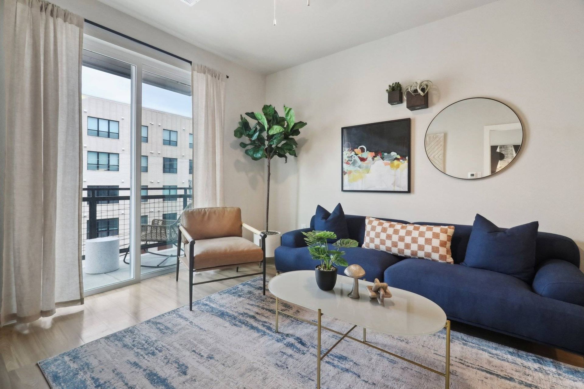Living room in a modern apartment with a navy sofa, beige chair, coffee table, and balcony doors.