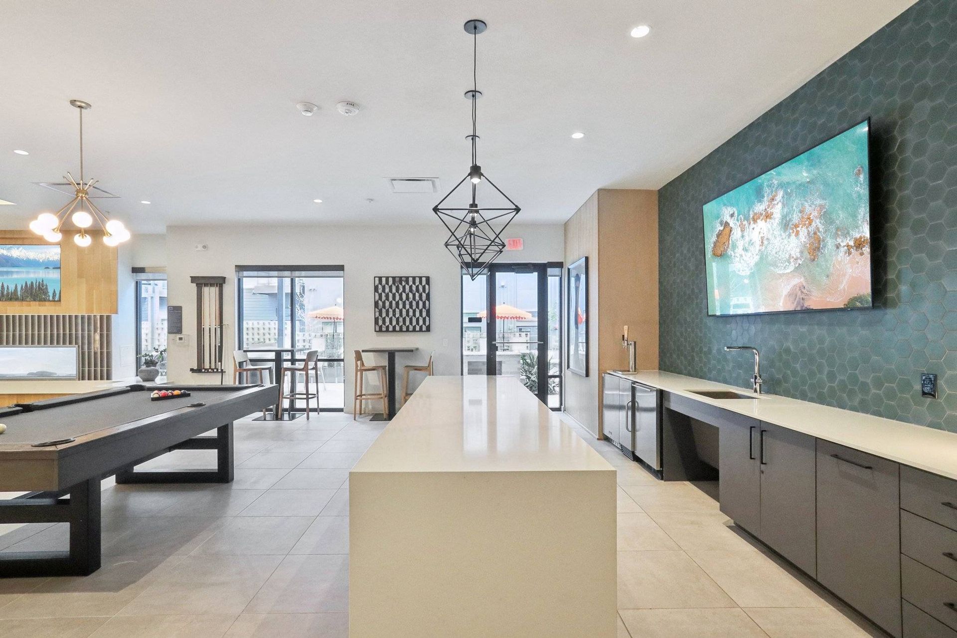 Modern community lounge with a long white island, pool table, and wall-mounted TV.