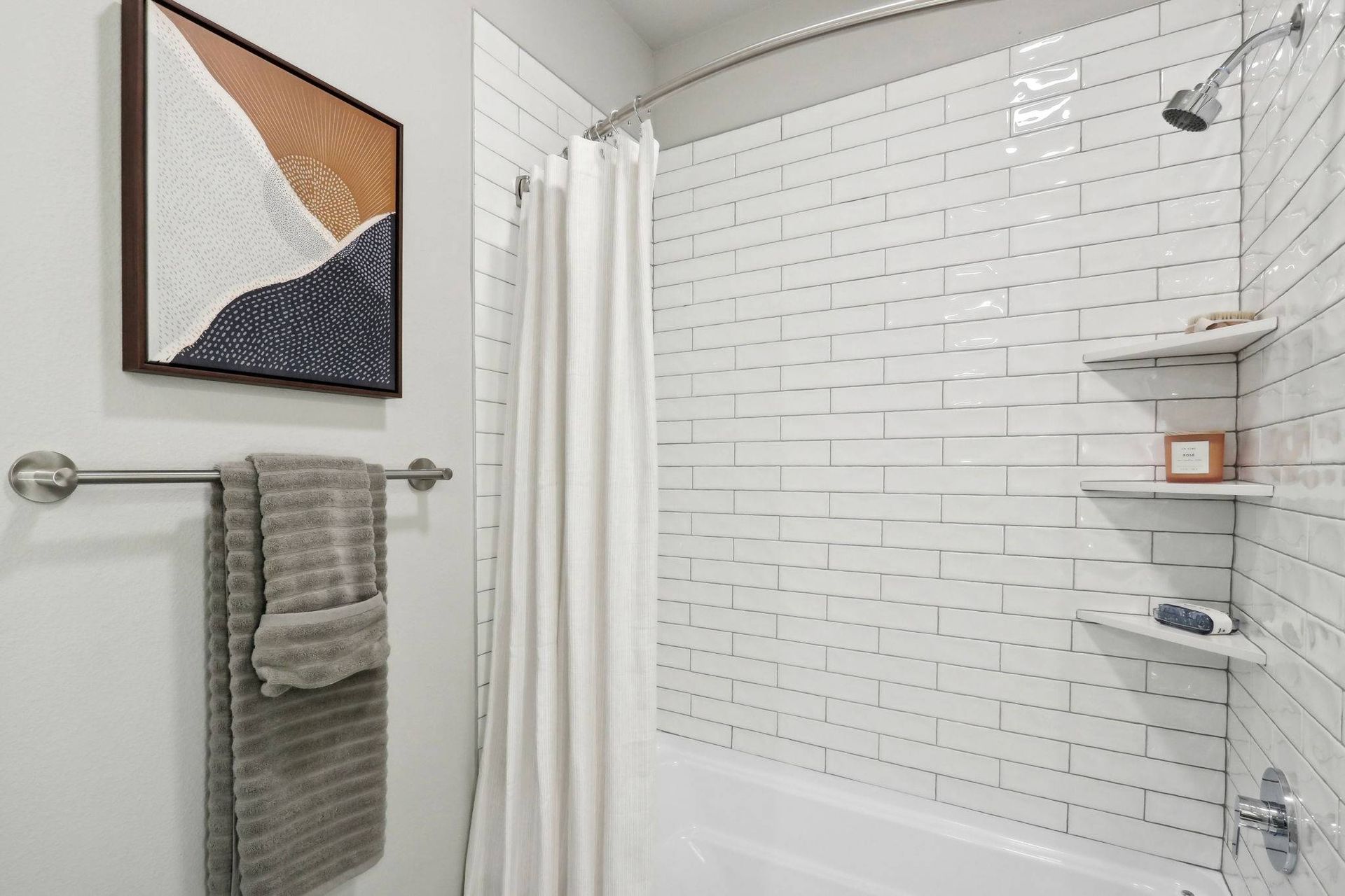 Bathroom with white subway tile walls, curved shower rod, shower curtain, towel bar, and wall shelves.
