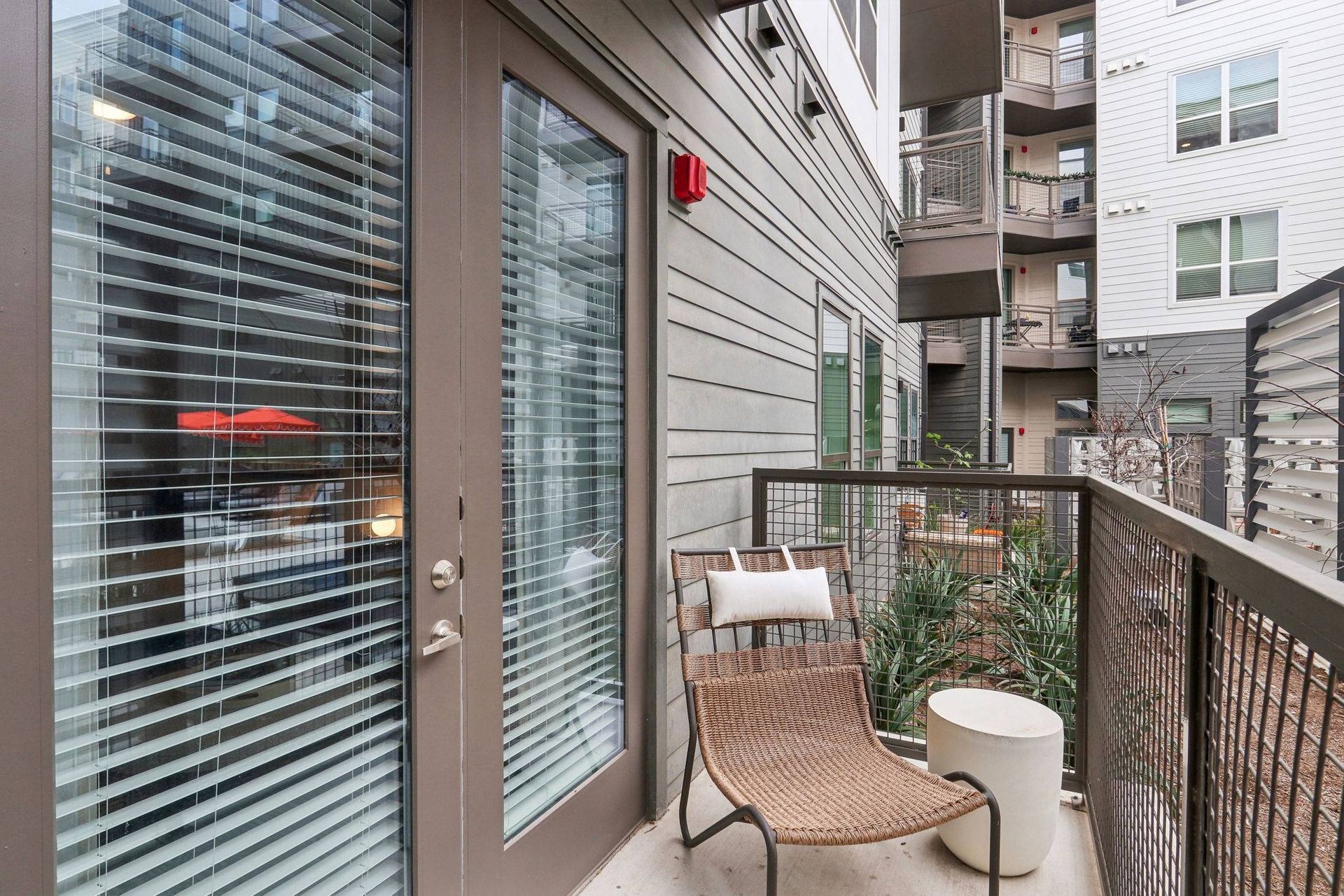 Apartment balcony with wicker chair, small white table, glass door, and railing.