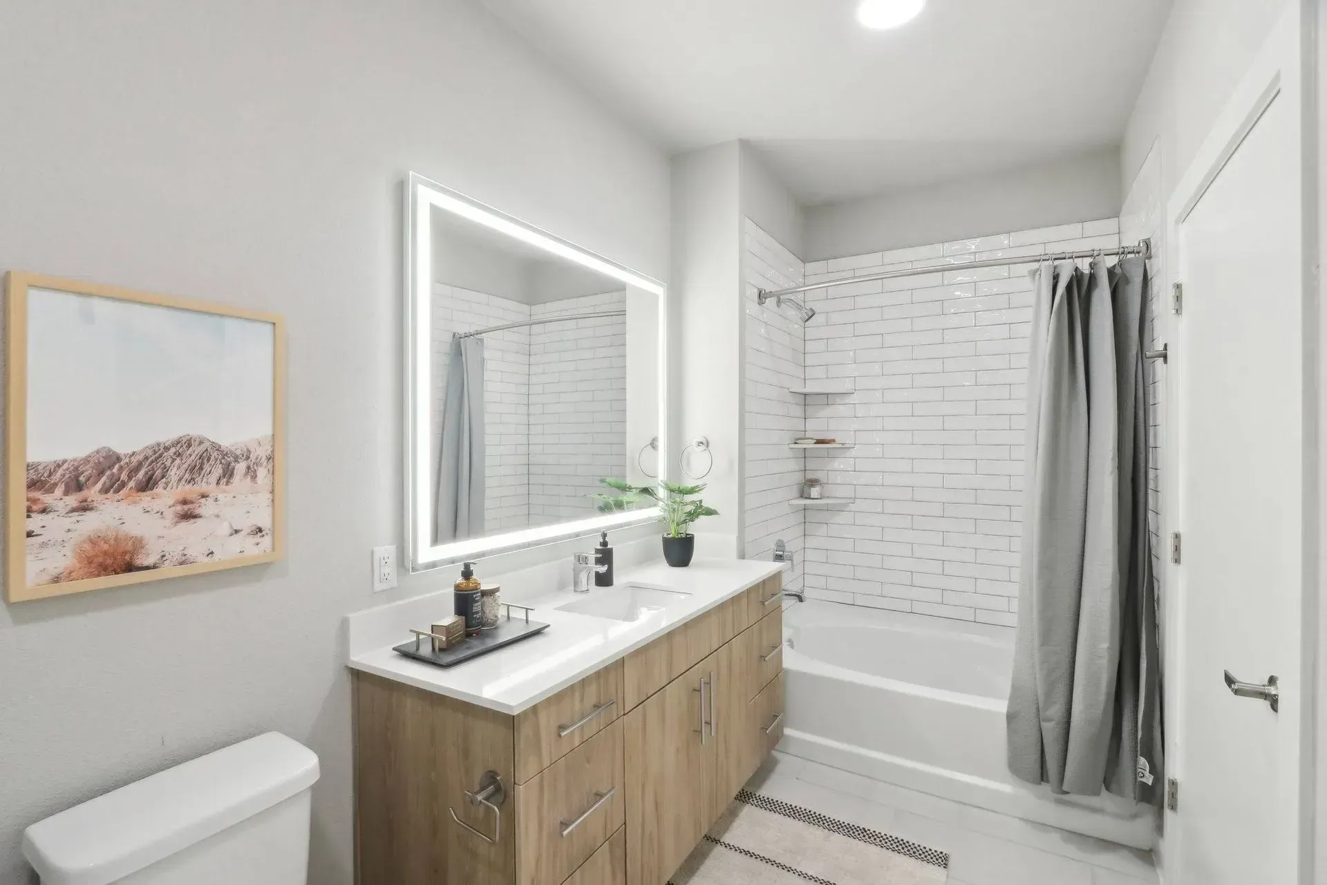 Modern bathroom with wooden vanity, large mirror, and white tiled tub/shower.