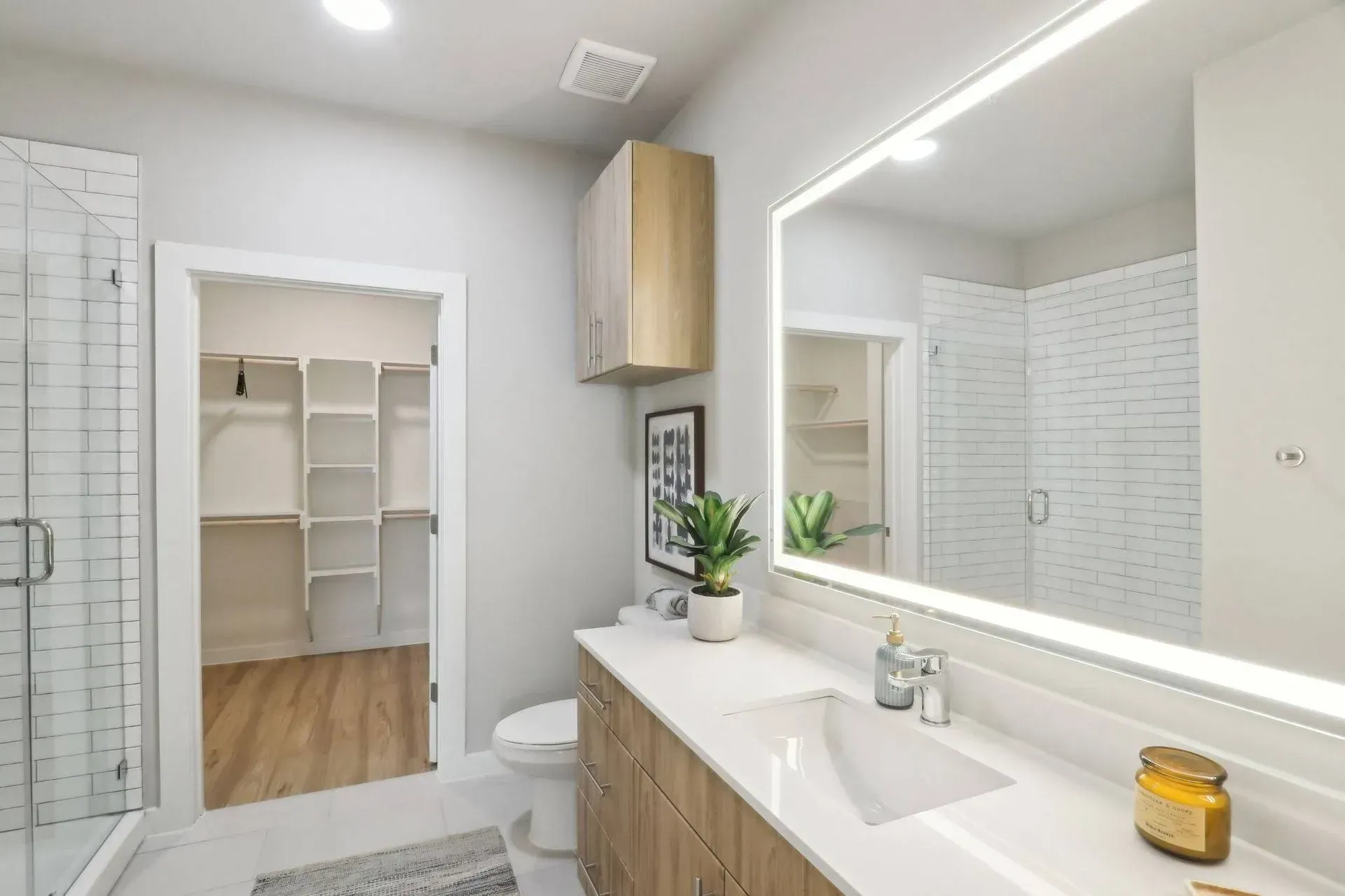 Modern bathroom with white walls, wood vanity, walk-in closet, and a large mirror.