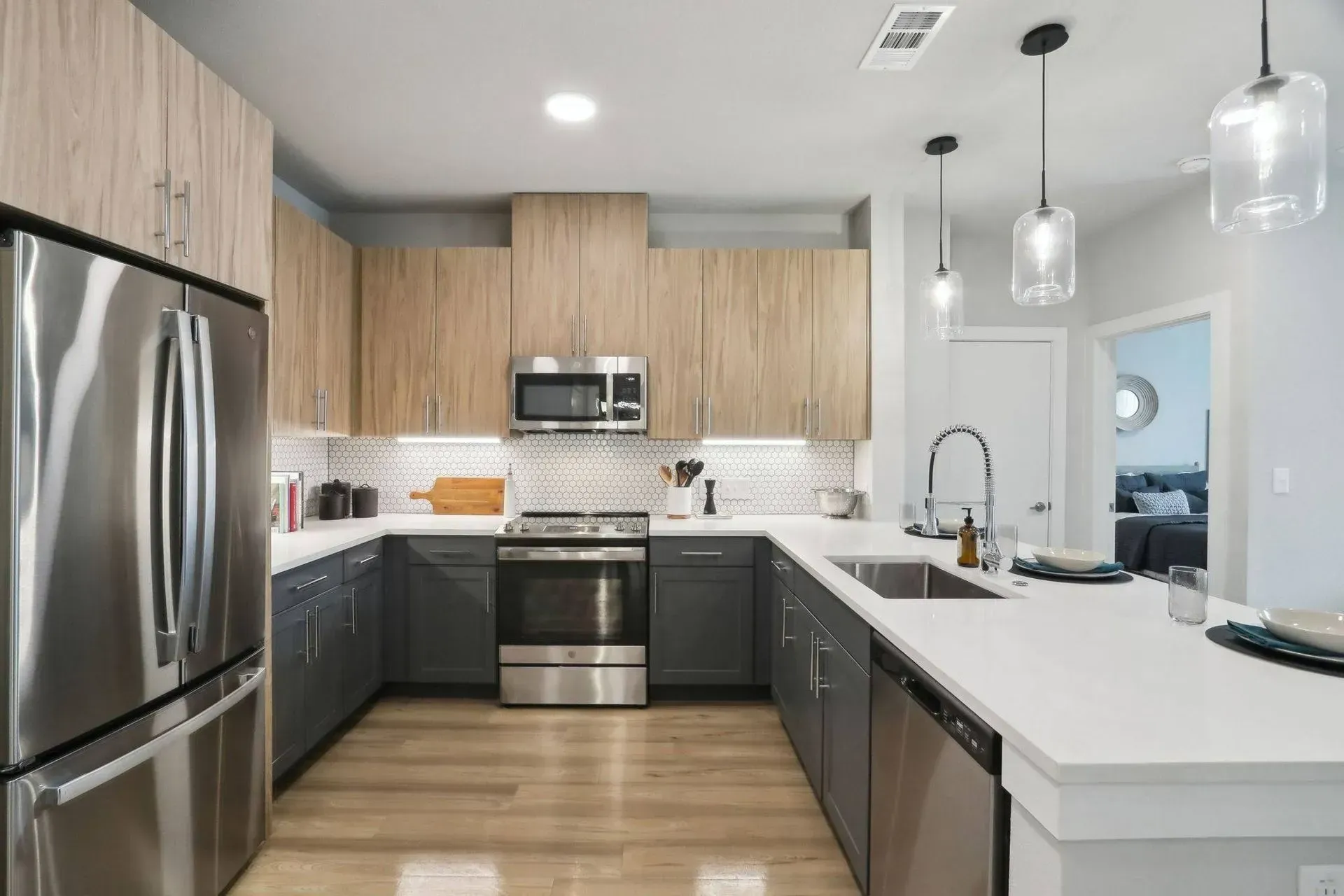 Modern kitchen with stainless steel appliances, two-tone cabinets, white countertops, and wood flooring.