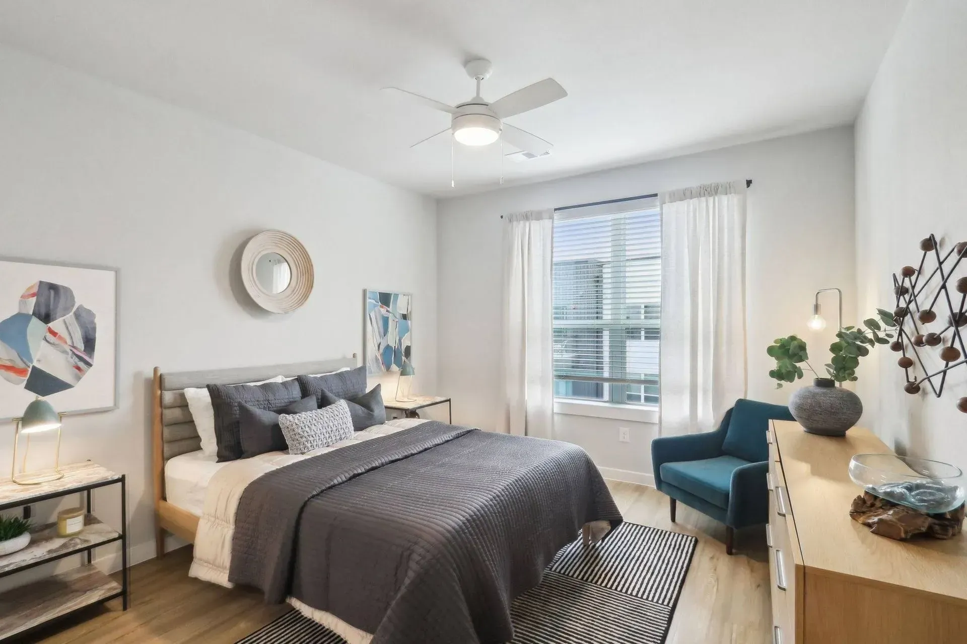 Bedroom with bed, dresser, chair, window, and decorative art. Soft colors, natural light.