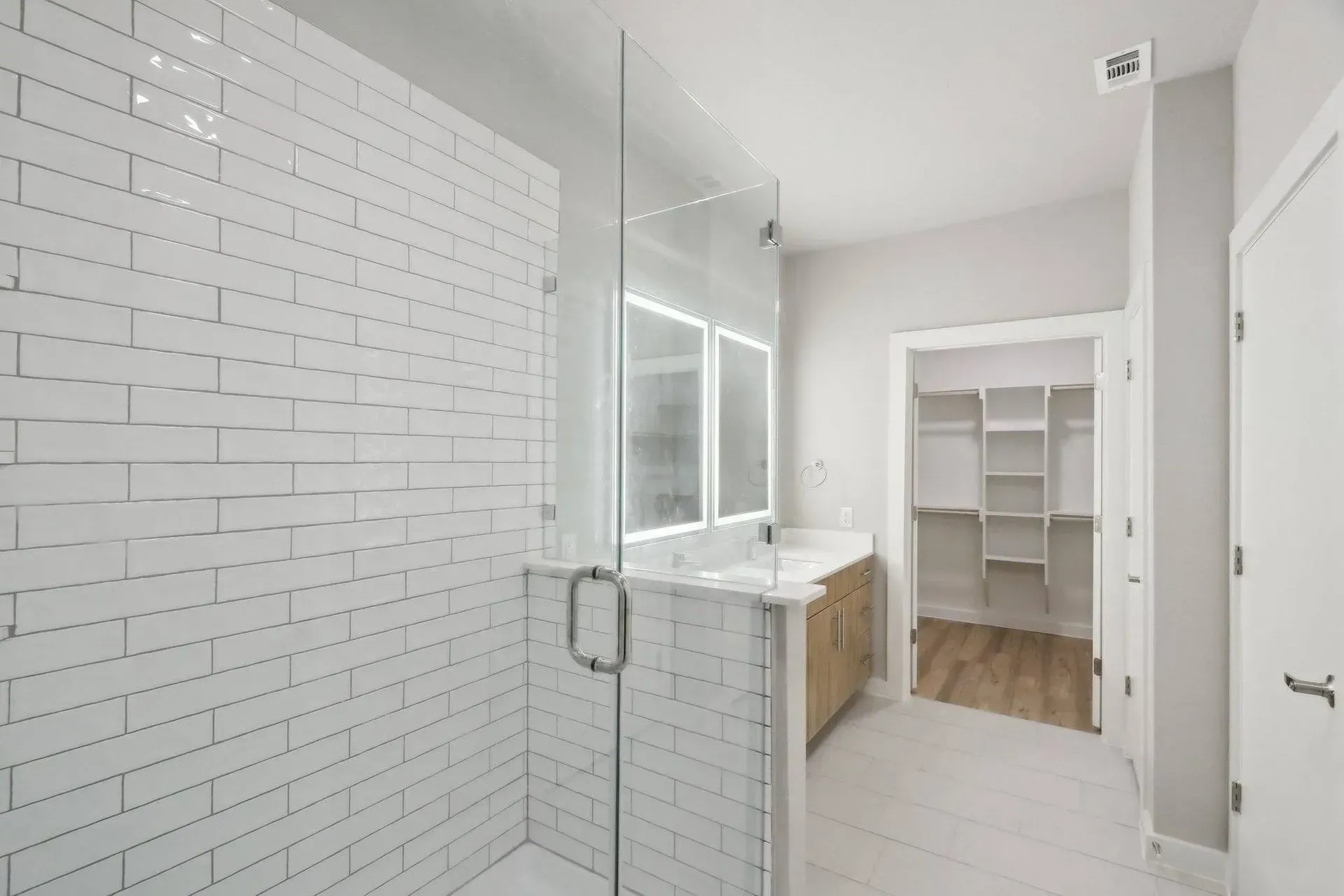 Modern bathroom with white subway tile shower, glass door, vanity, and walk-in closet.