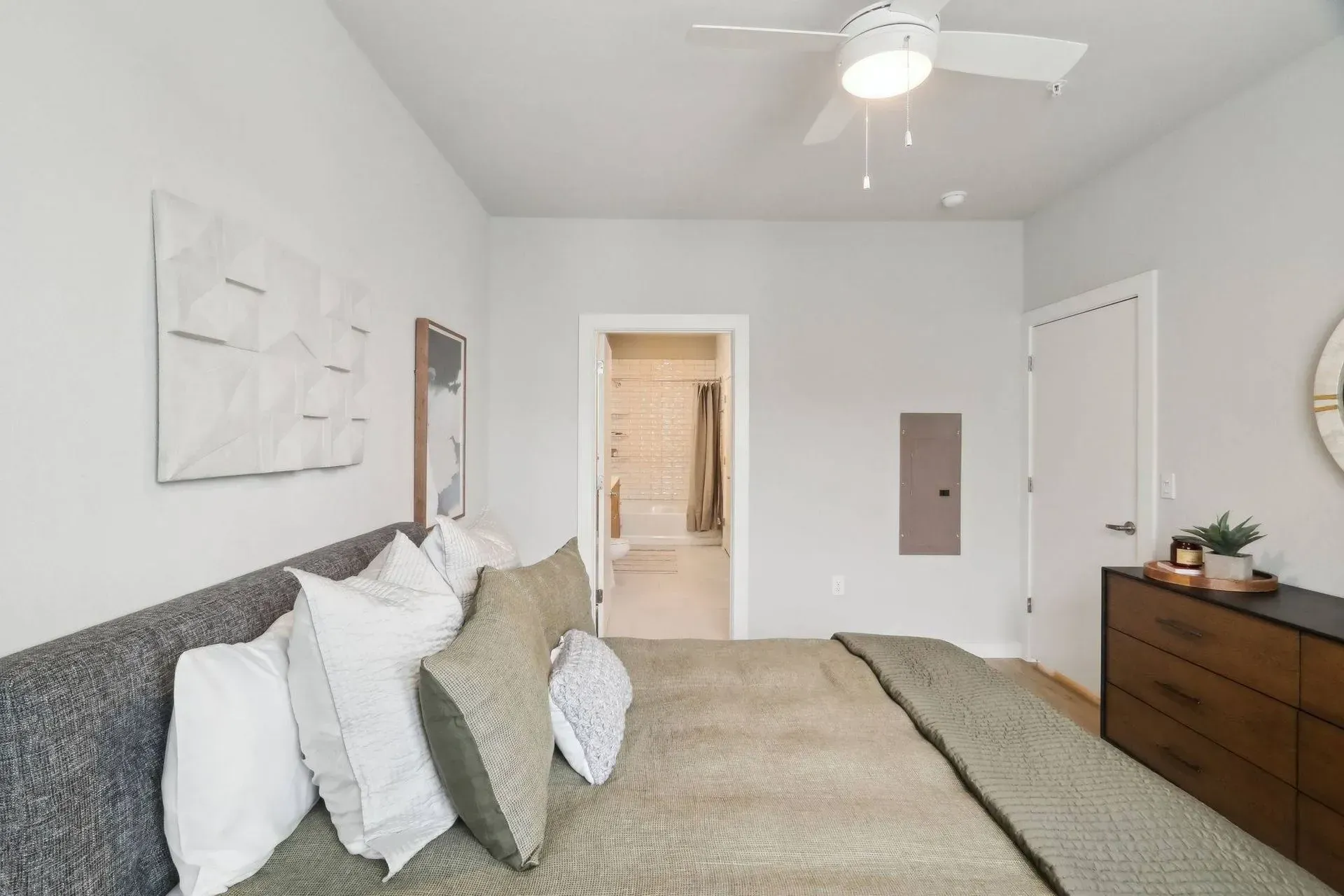 Bedroom with bed, pillows, dresser, artwork, door to bathroom, and ceiling fan.