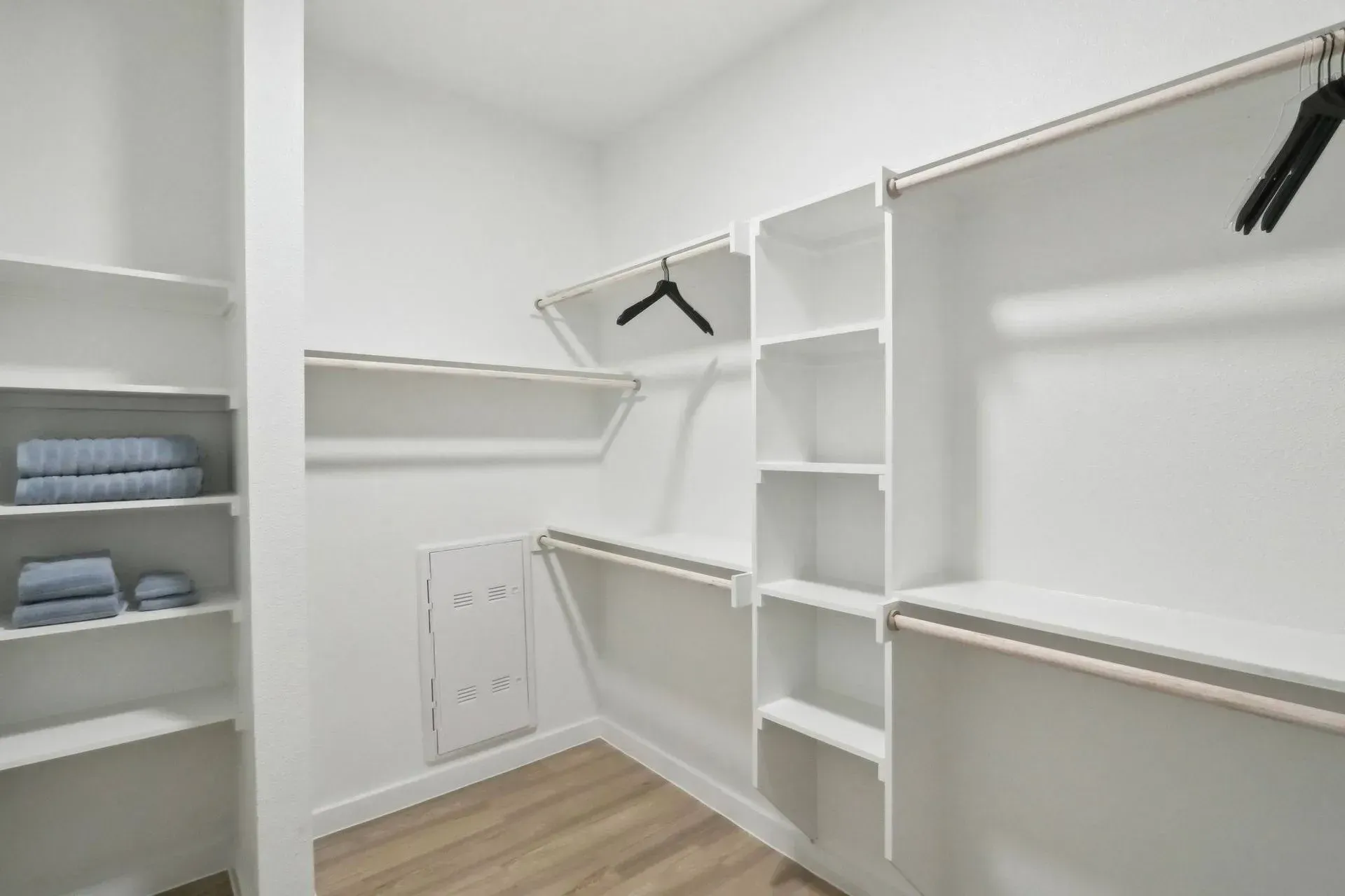 White walk-in closet with shelves and rods; towels on left shelves.