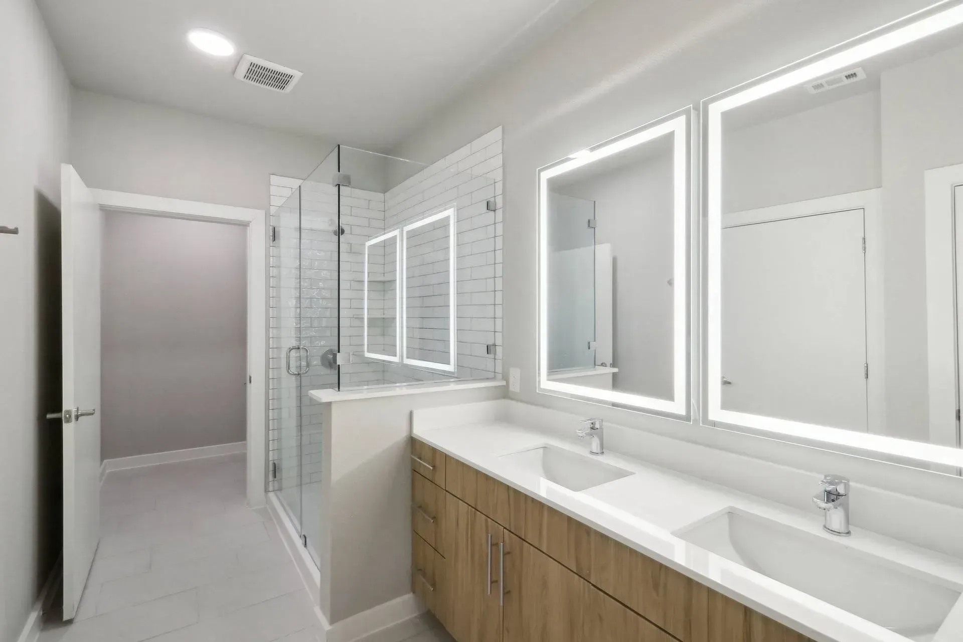 Modern bathroom with double vanity, large mirrors, glass shower, and wood cabinets.