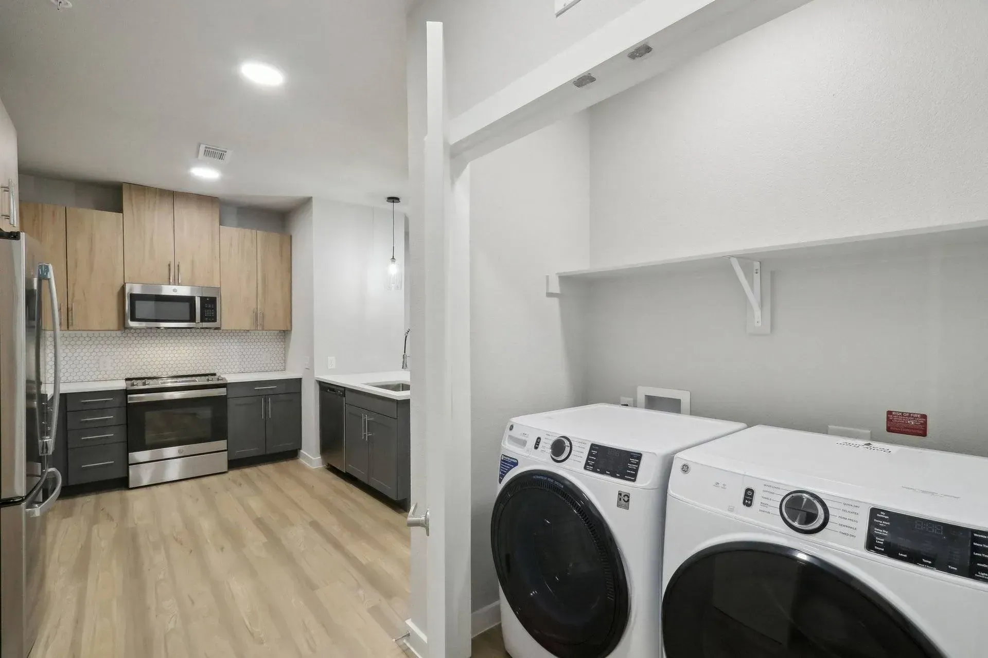 A laundry area with white washer and dryer, adjacent to a kitchen with wood cabinets and stainless steel appliances.