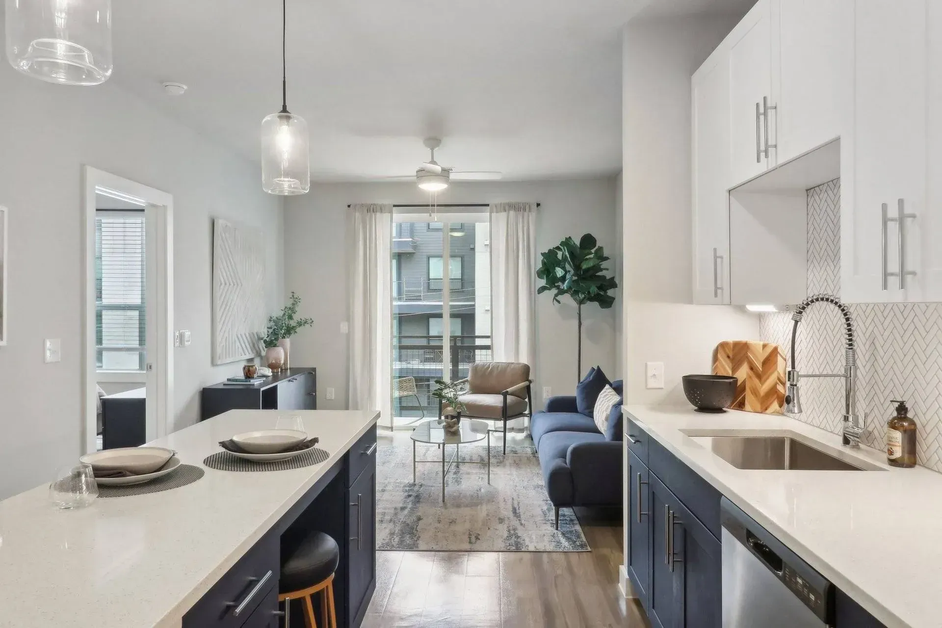Modern apartment interior: kitchen with island, living room with blue sofa, large windows, neutral colors.