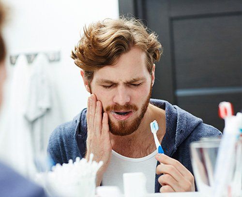 Young guy in pain holding his jaw after brushing teeth