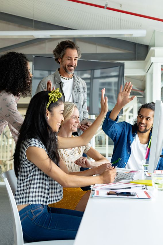 Een groep mensen die rond een tafel zitten, geeft elkaar een high five.