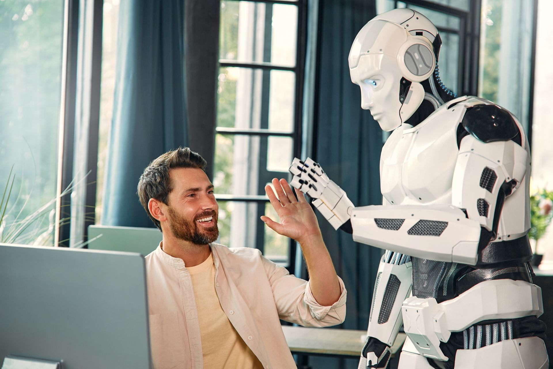 Een man geeft een high five aan een robot terwijl hij achter een computer zit.