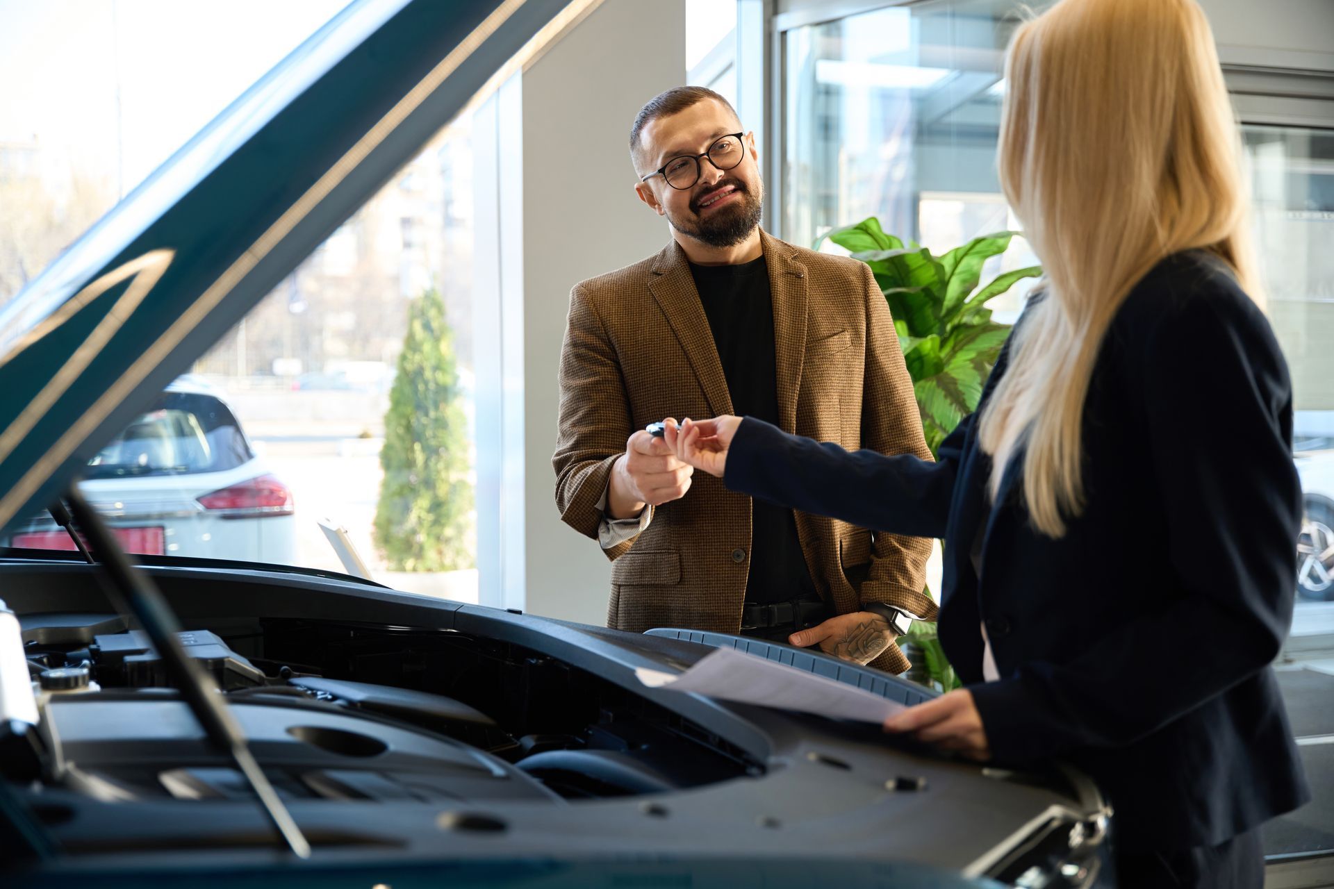 Een man en een vrouw schudden elkaar de hand voor een auto in een showroom.