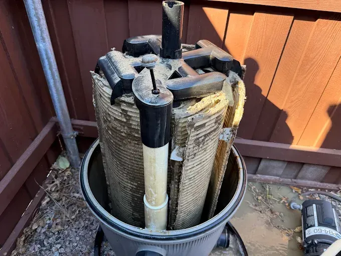 Pool filter cartridge pulled from its housing; brown pleated filter is caked with dirt and debris.