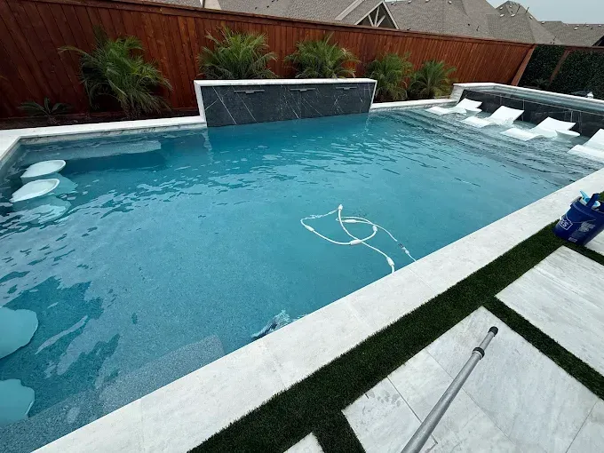 A swimming pool with clear turquoise water, a waterfall feature, and surrounding patio with artificial grass.