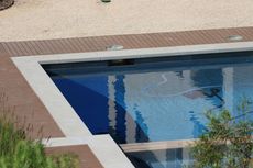 A top-down view of a swimming pool with blue water. A robotic cleaner and a section of the pool's tiled floor is visible.