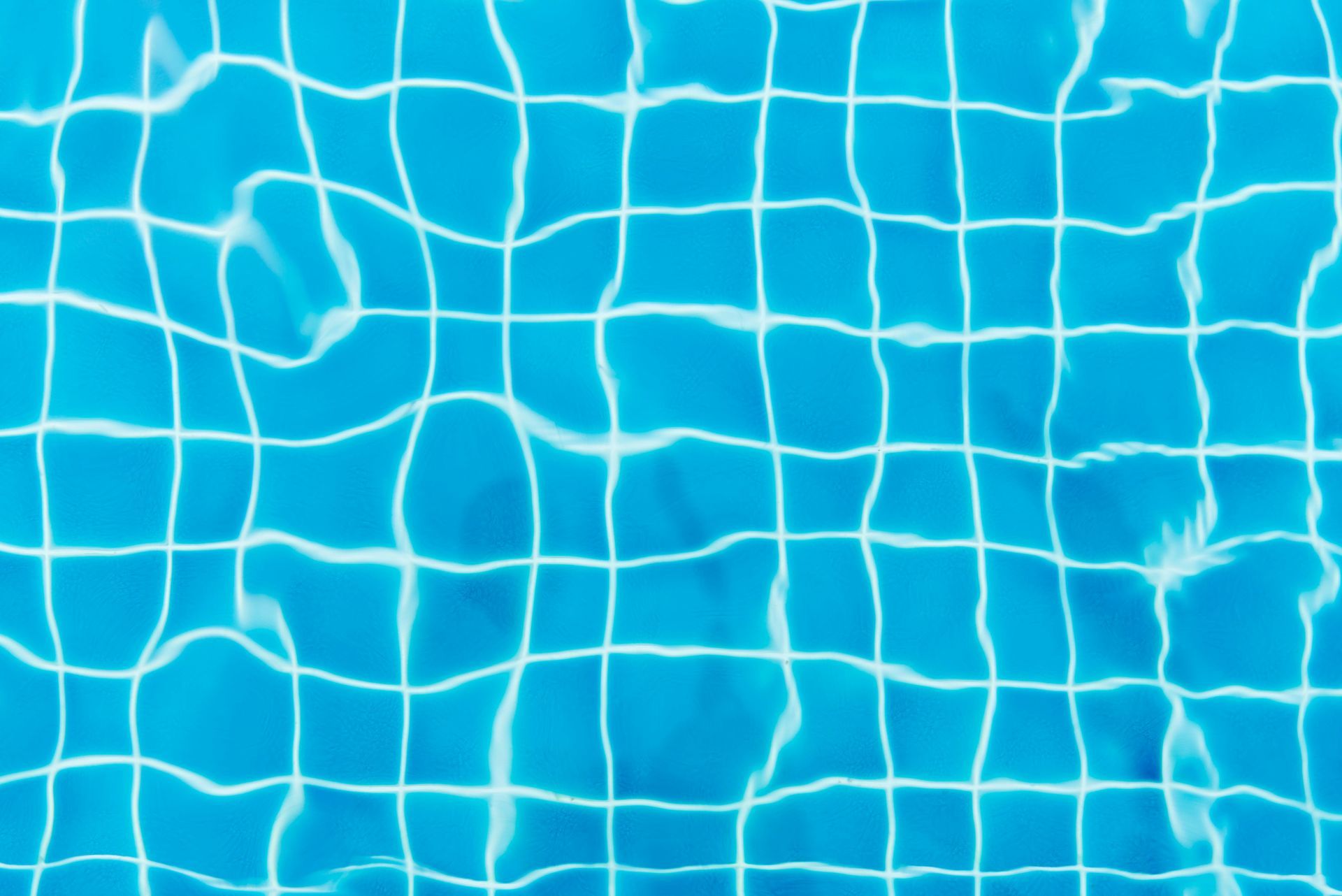 Blue swimming pool water with visible grid lines of the tiled floor, slightly distorted by the water's surface.